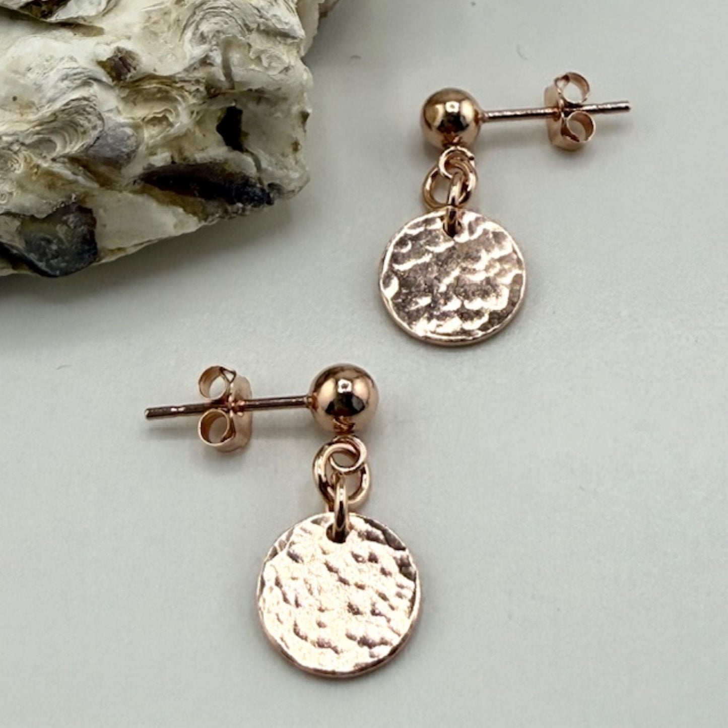 Rose gold stud earrings with circular discs on a light gray background