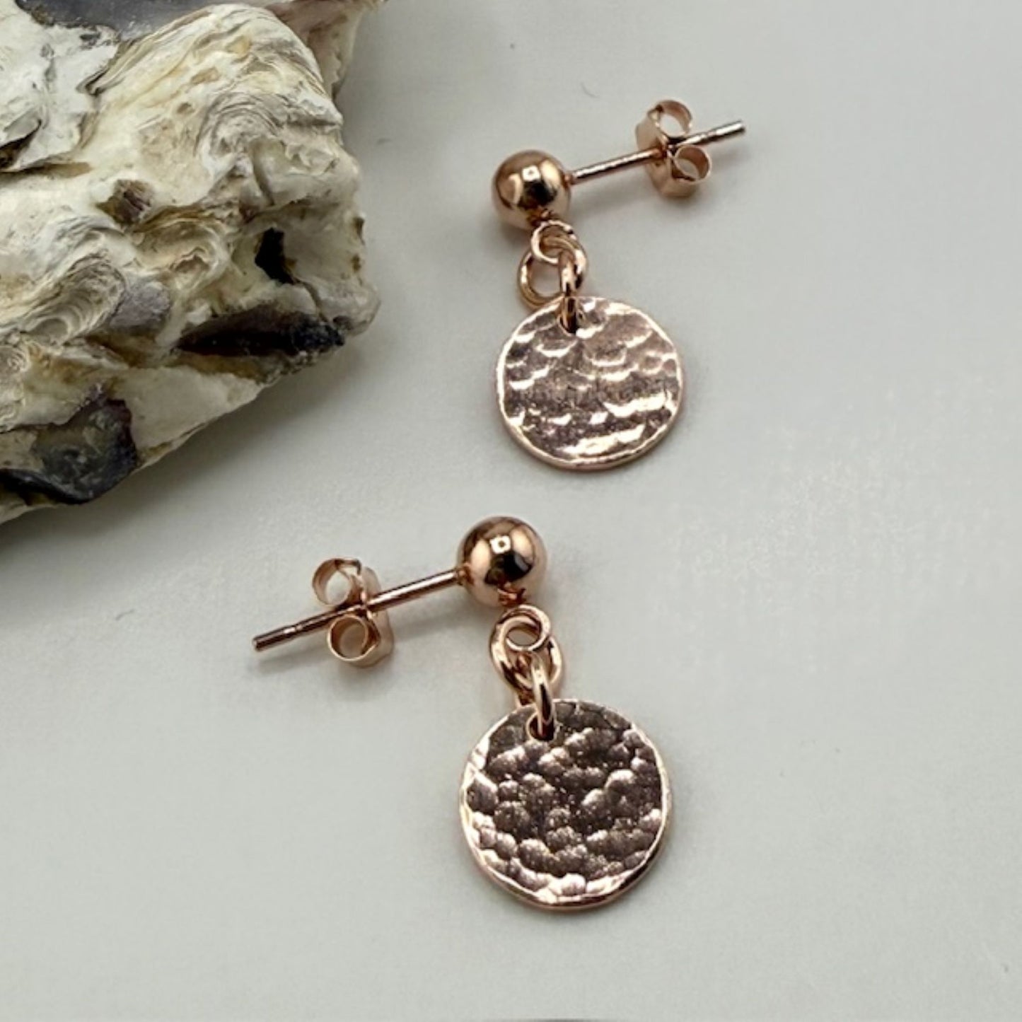 Rose gold stud earrings with round discs on a light gray background