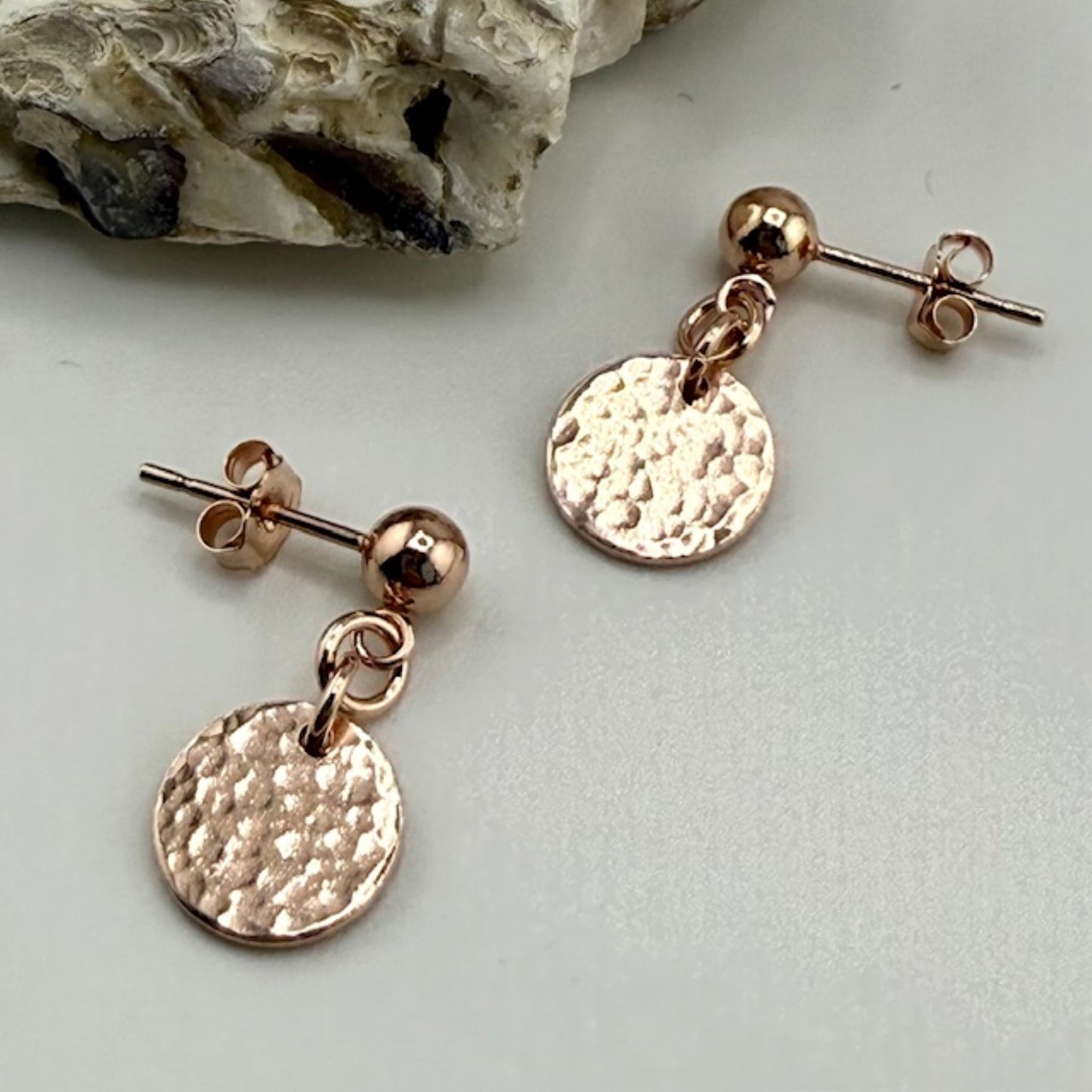 Rose gold stud earrings with round discs on a light gray background