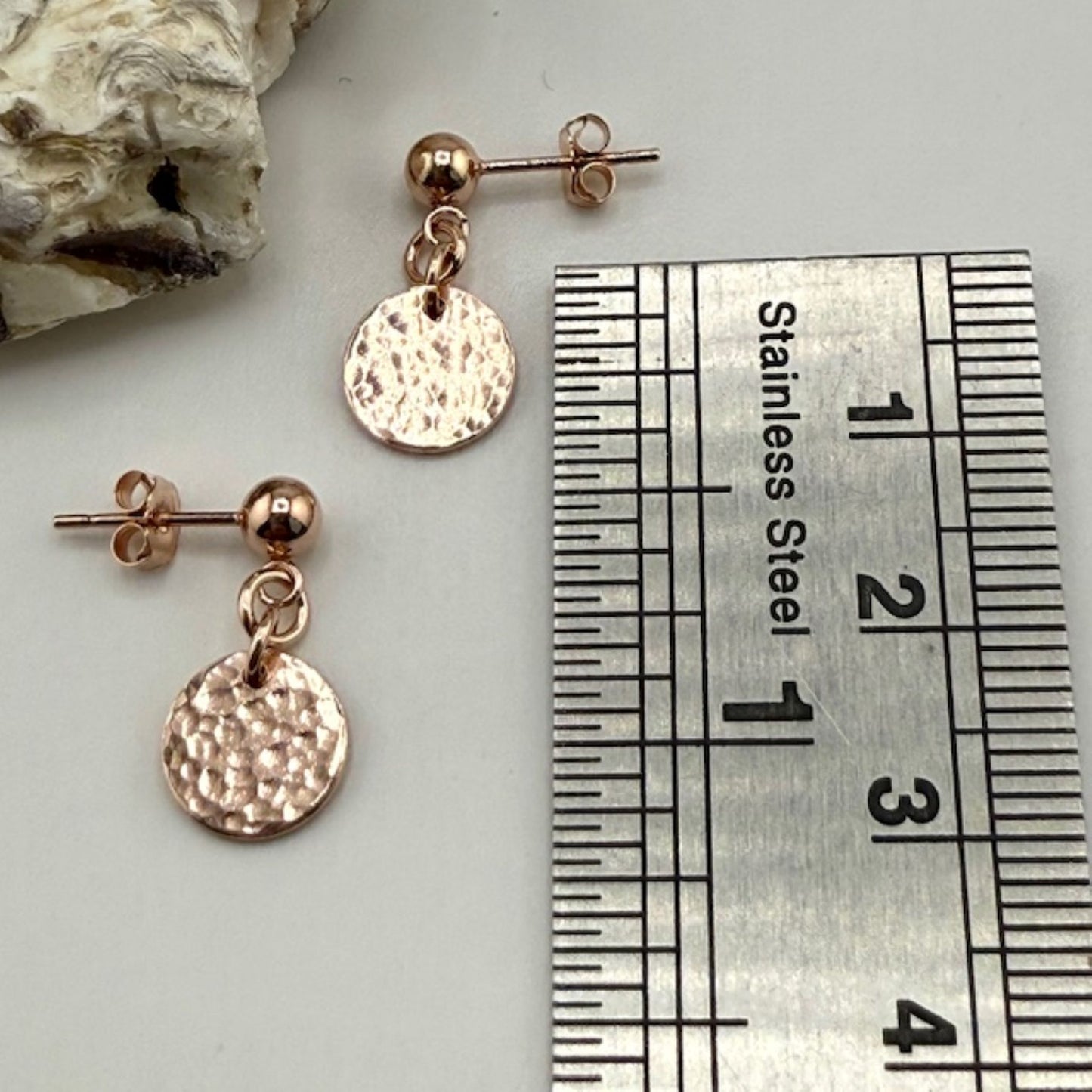 Rose gold stud earrings with round discs next to a ruler for size reference.