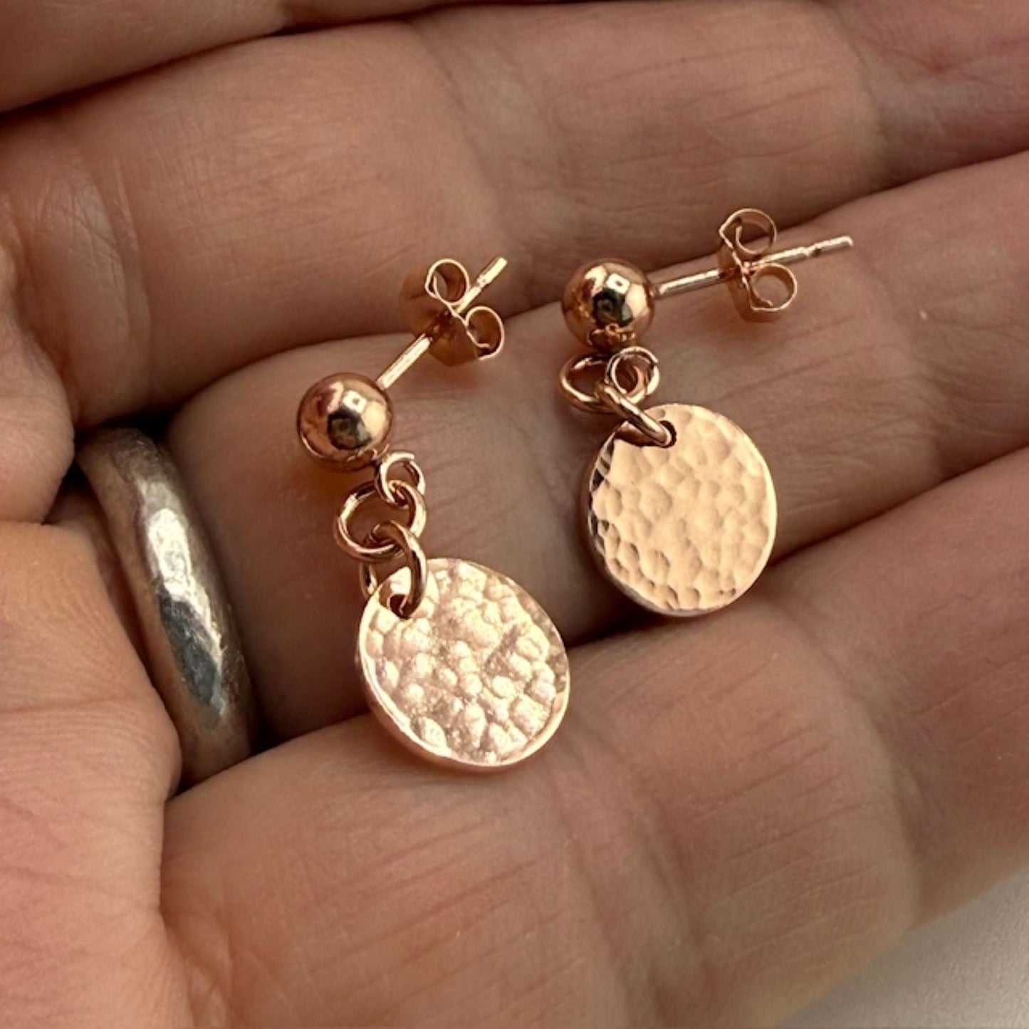 Rose gold stud earrings with round discs held between fingers