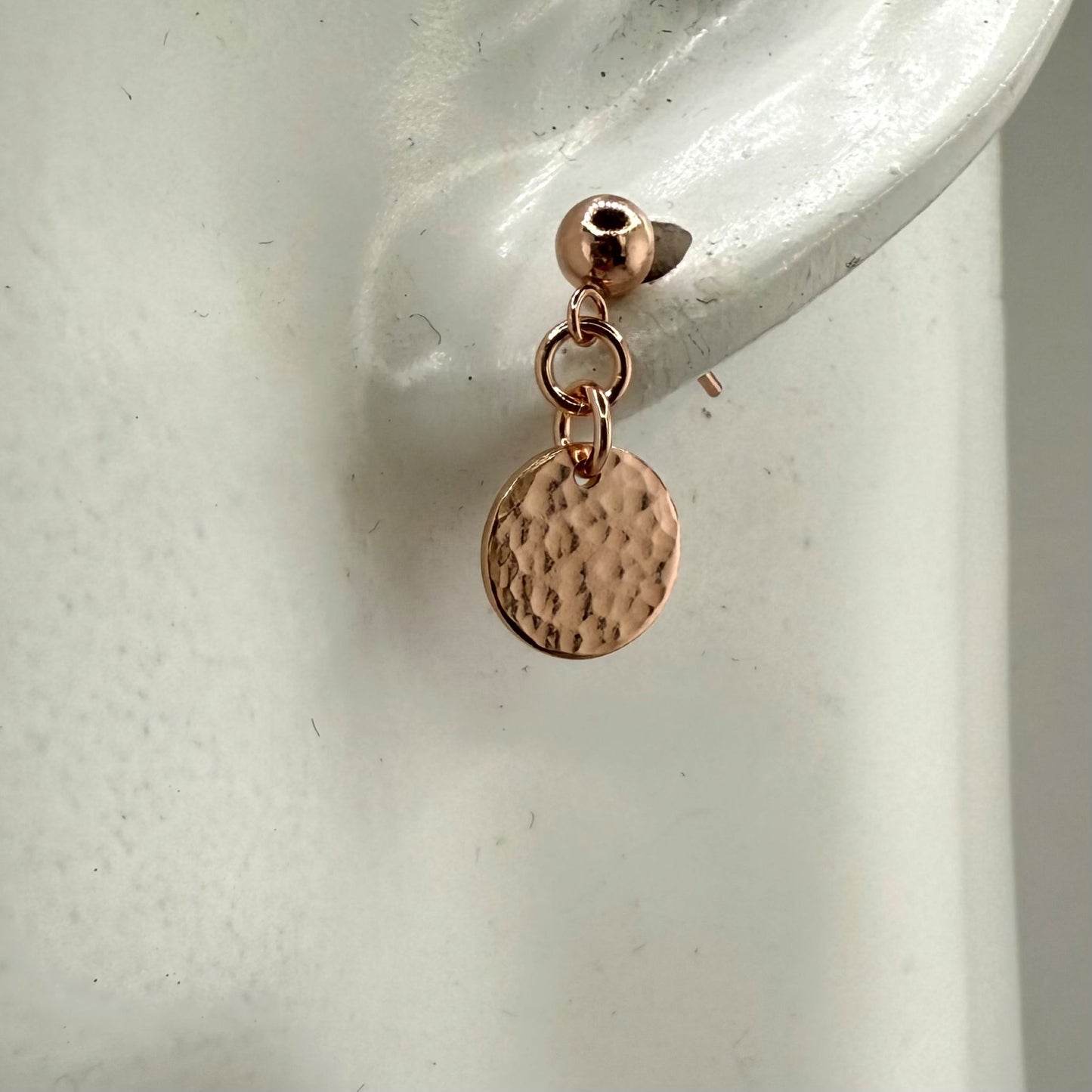 Rose gold stud earring with a round discs on a display ear against a neutral background