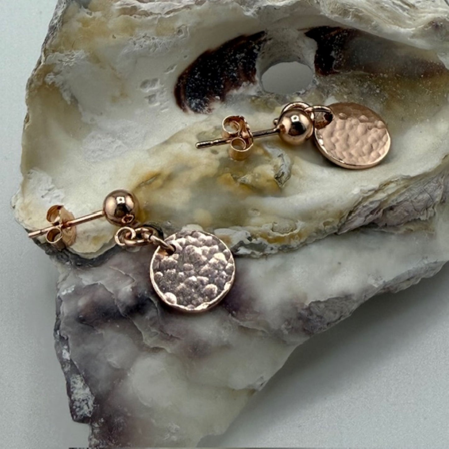 Rose gold studs earrings with round discs on a textured stone surface
