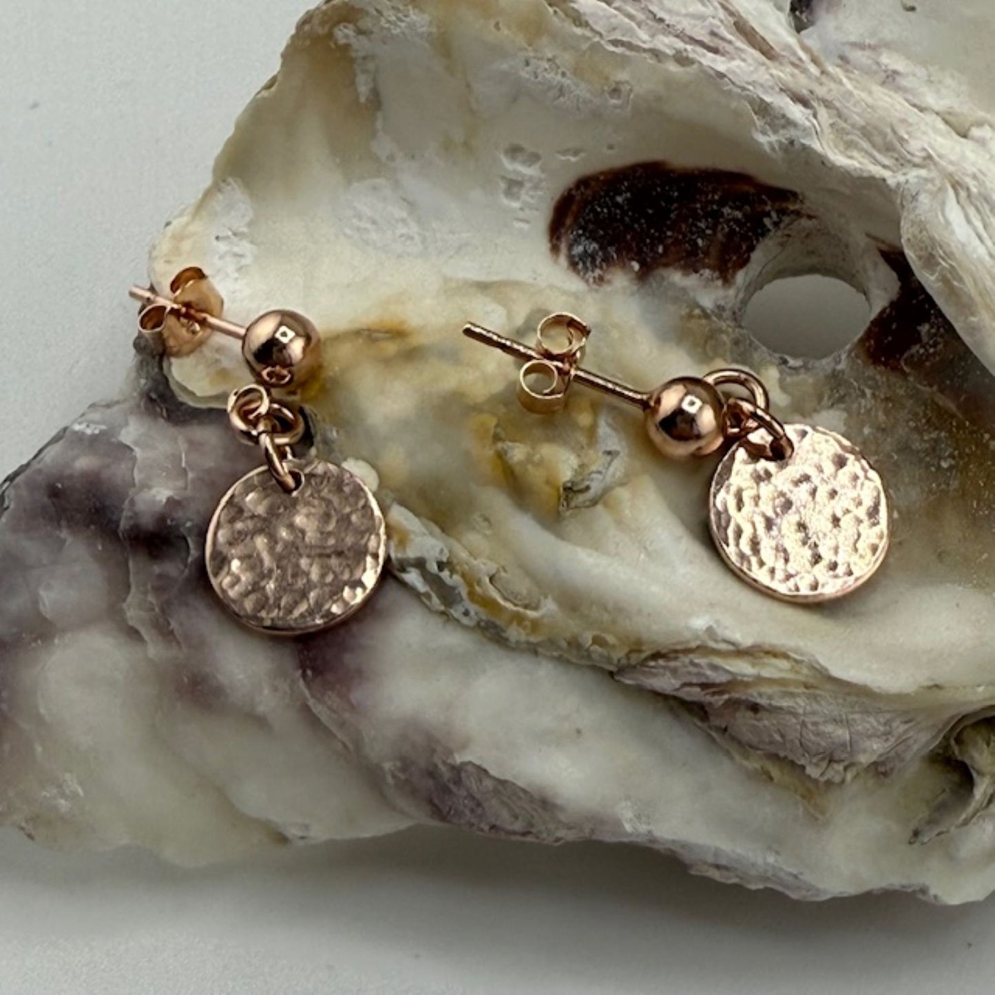 Rose gold stud earrings with round discs on a textured stone surface