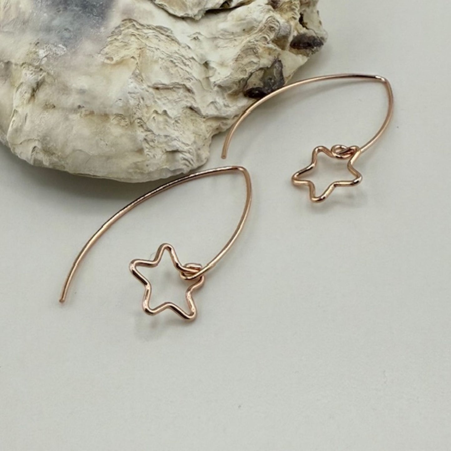 Rose gold star-shaped earrings on a light gray surface with a rock in the background
