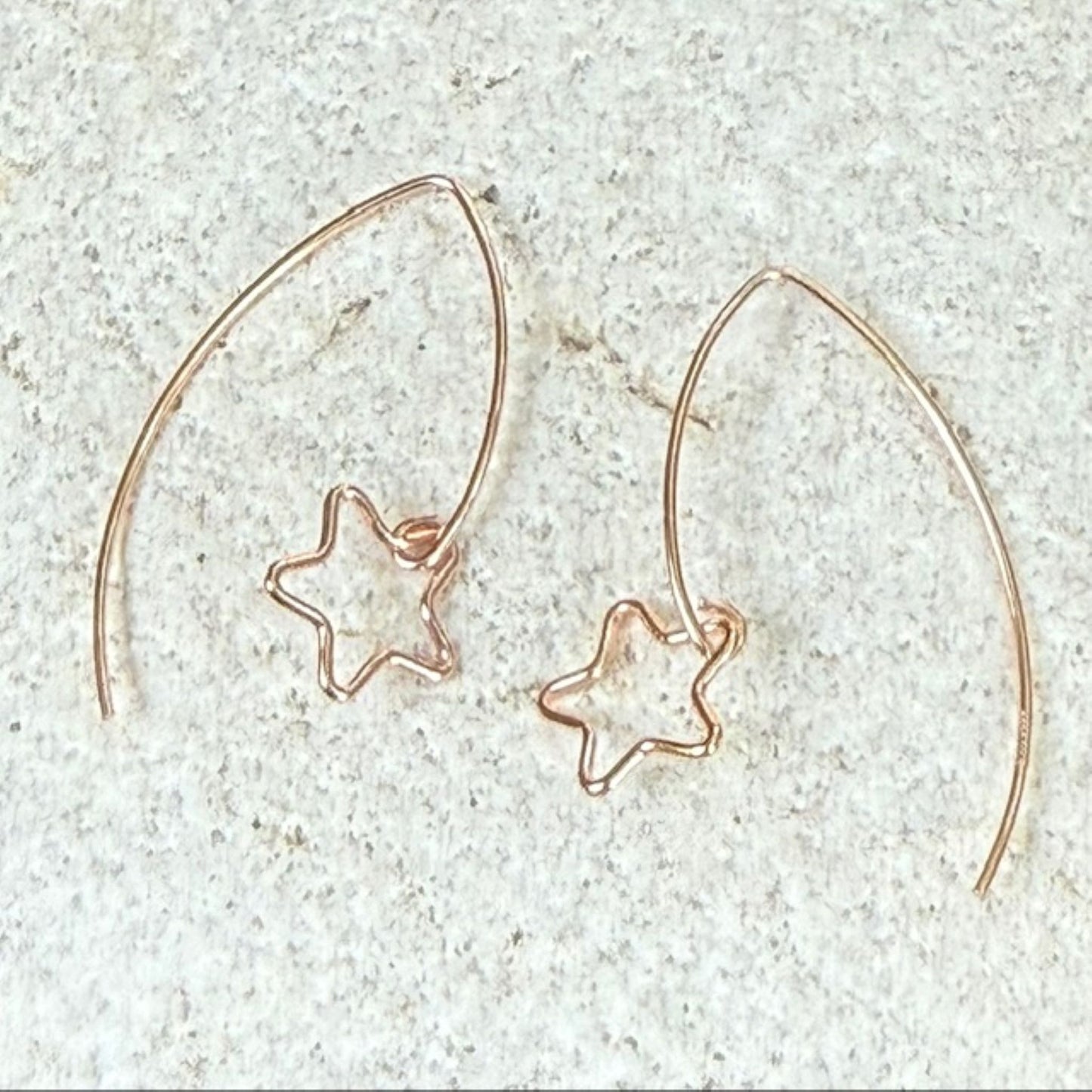 Rose gold hoop star earrings on a light stone background