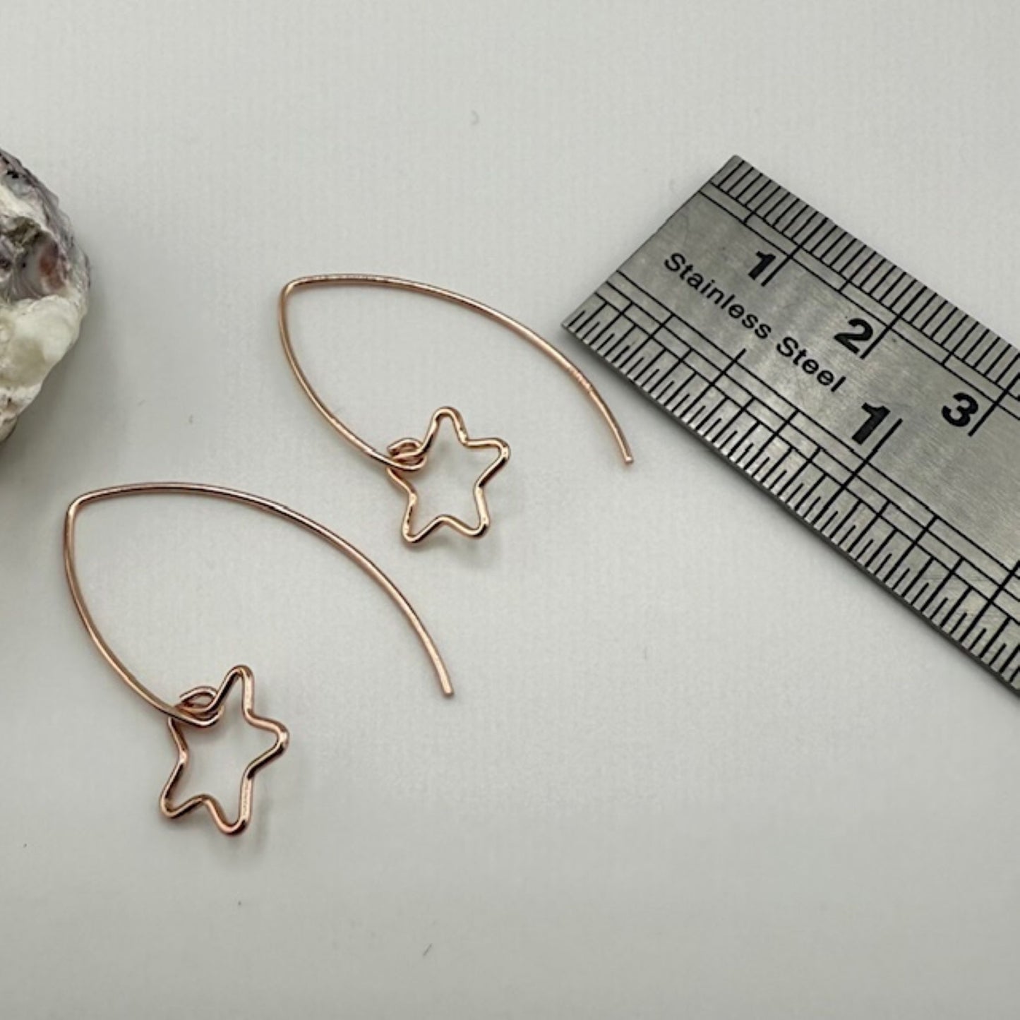 Rose gold star-shaped earrings with a ruler for scale on a light gray background