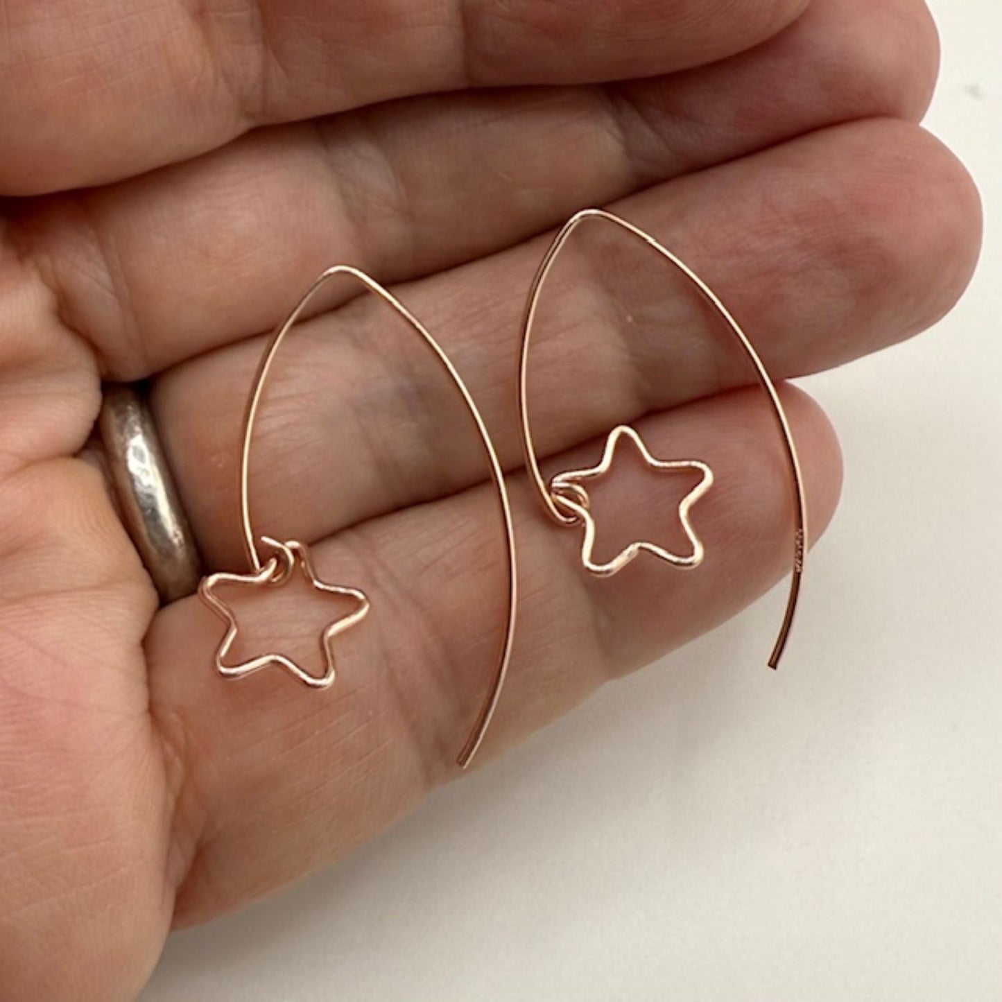 Rose gold hoop earrings with star details held between fingers on a light background