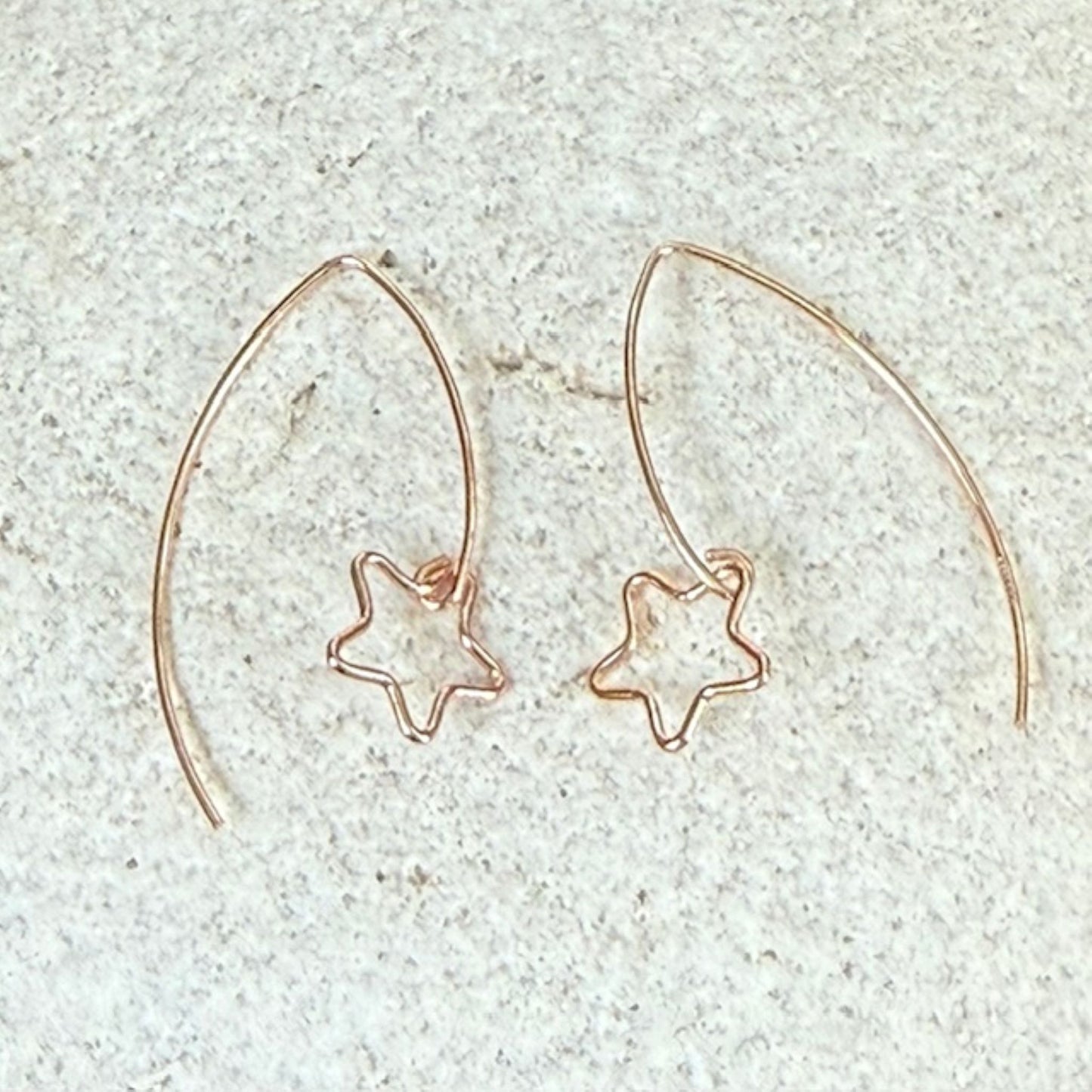 Rose gold star-shaped earrings on a light gray stone background