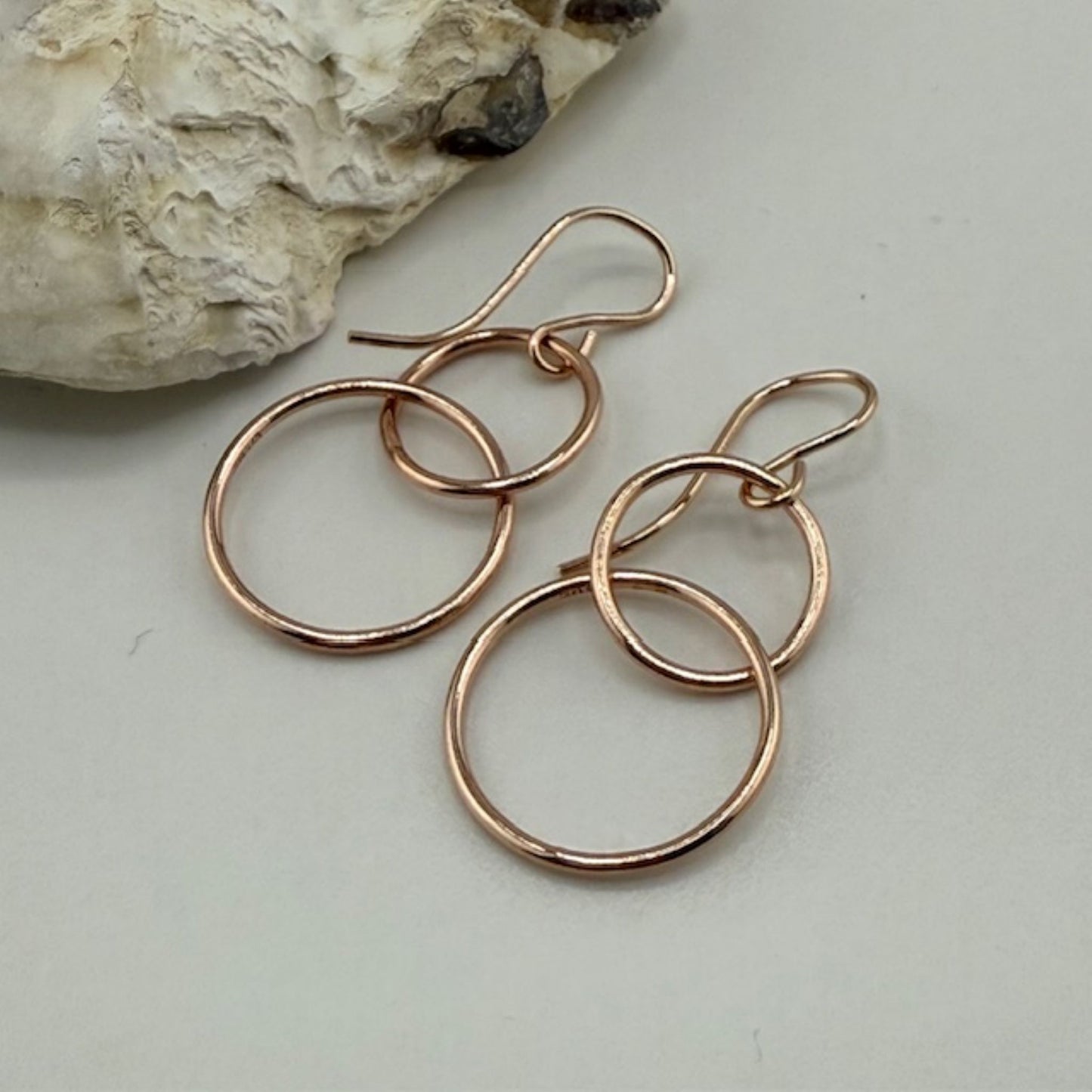 Rose gold hoop earrings on a light gray surface with a stone in the background
