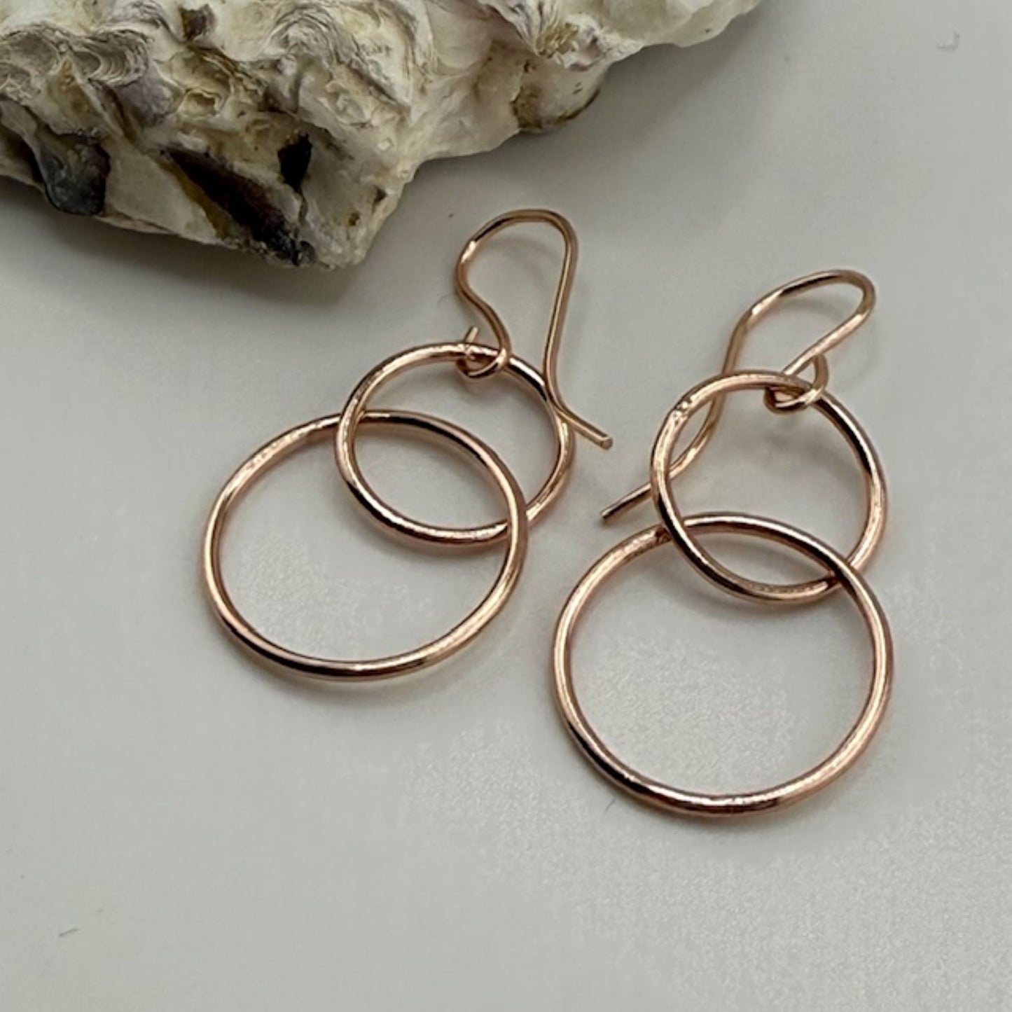 Pair of rose gold hoop earrings on a light gray surface with a stone in the background.