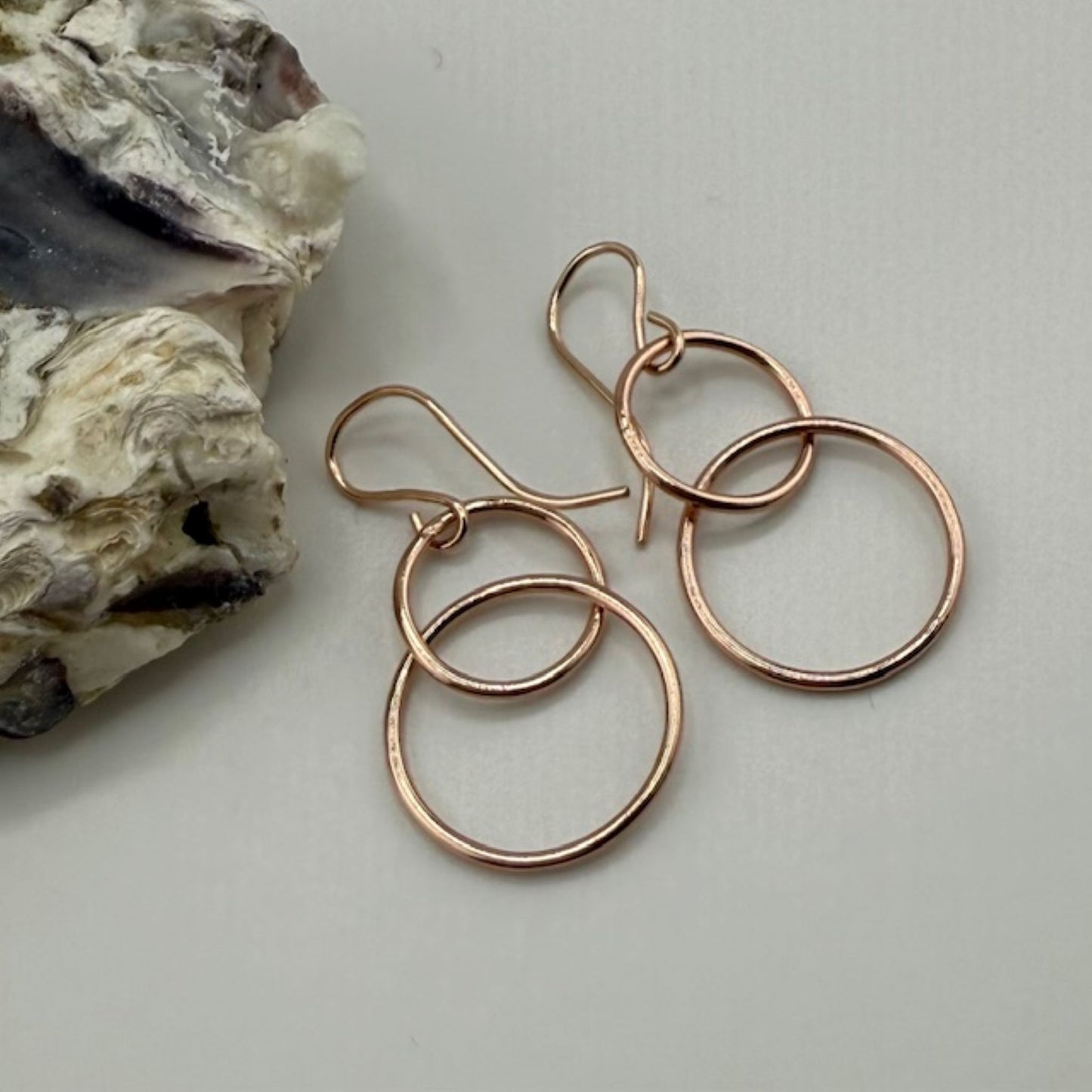 Rose gold hoop earrings on a light gray surface with a rock in the background