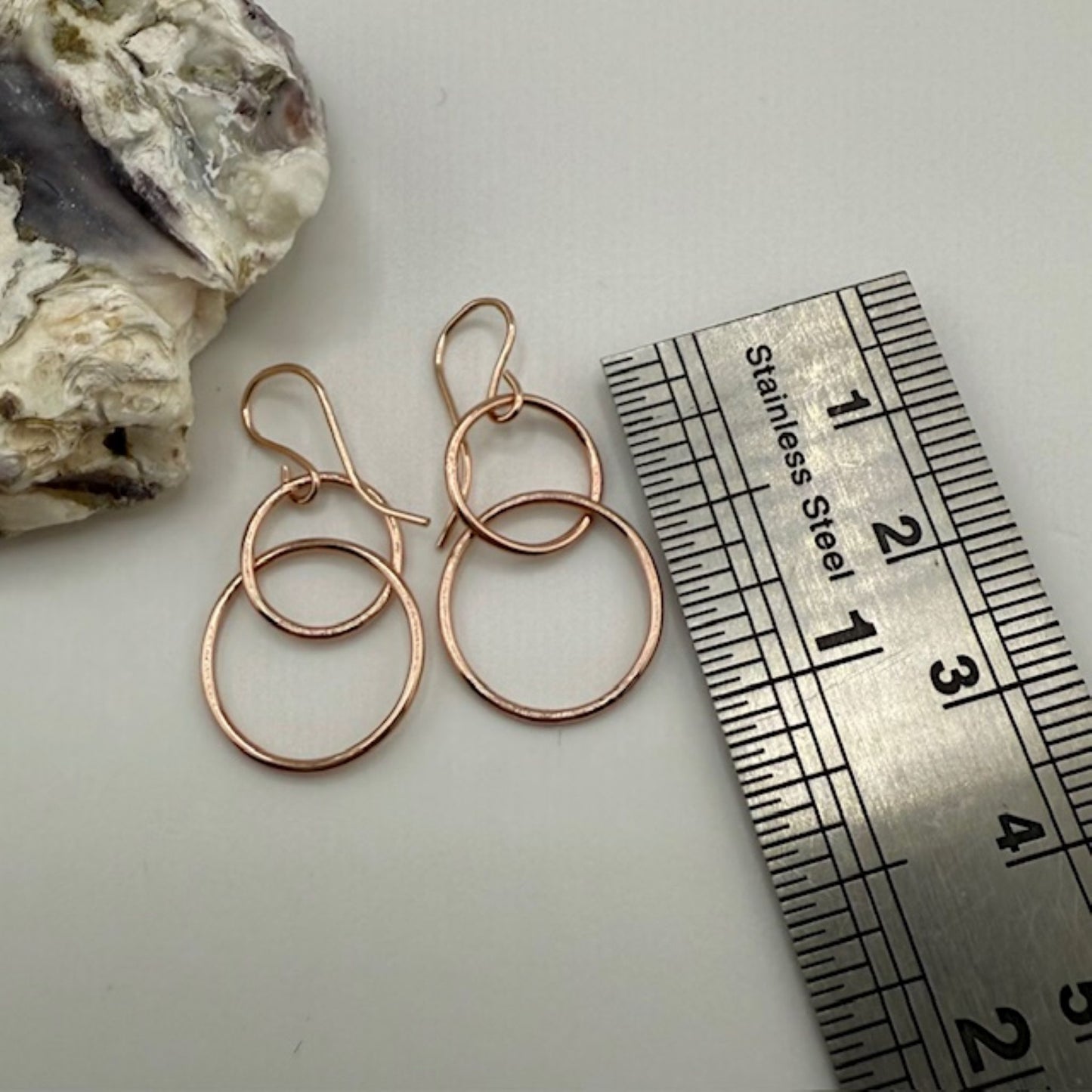 Rose gold hoop earrings with a ruler for scale on a light background
