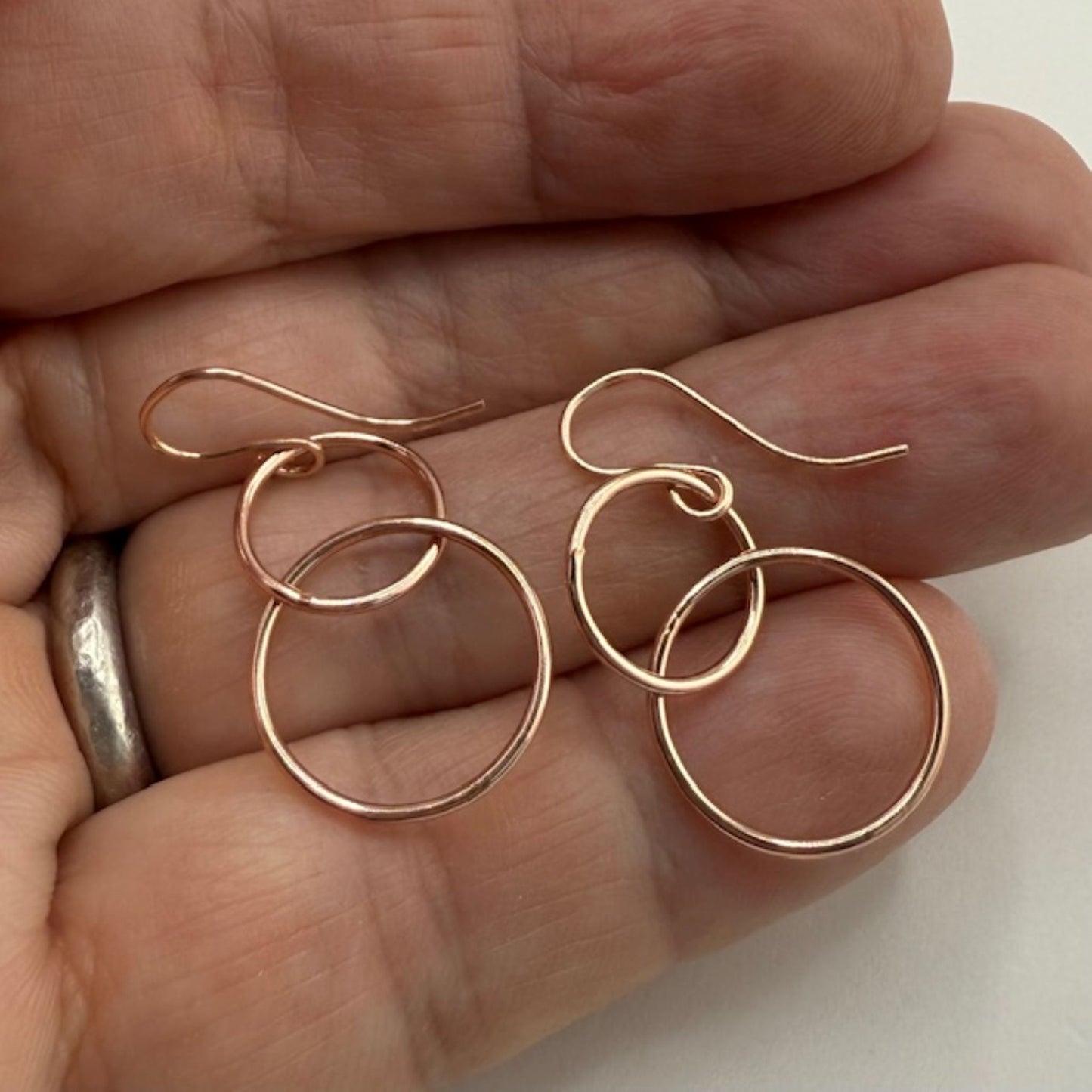 Rose gold hoop earrings held between fingers on a neutral background