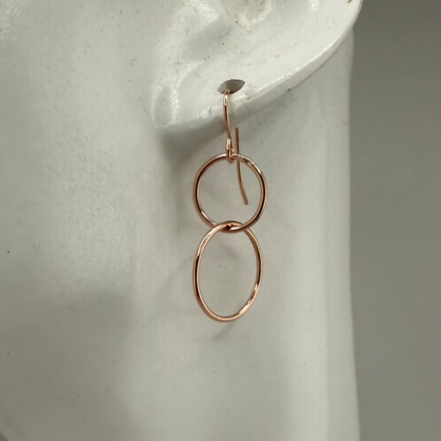 Rose gold double-circle earring on a white display stand with a neutral background
