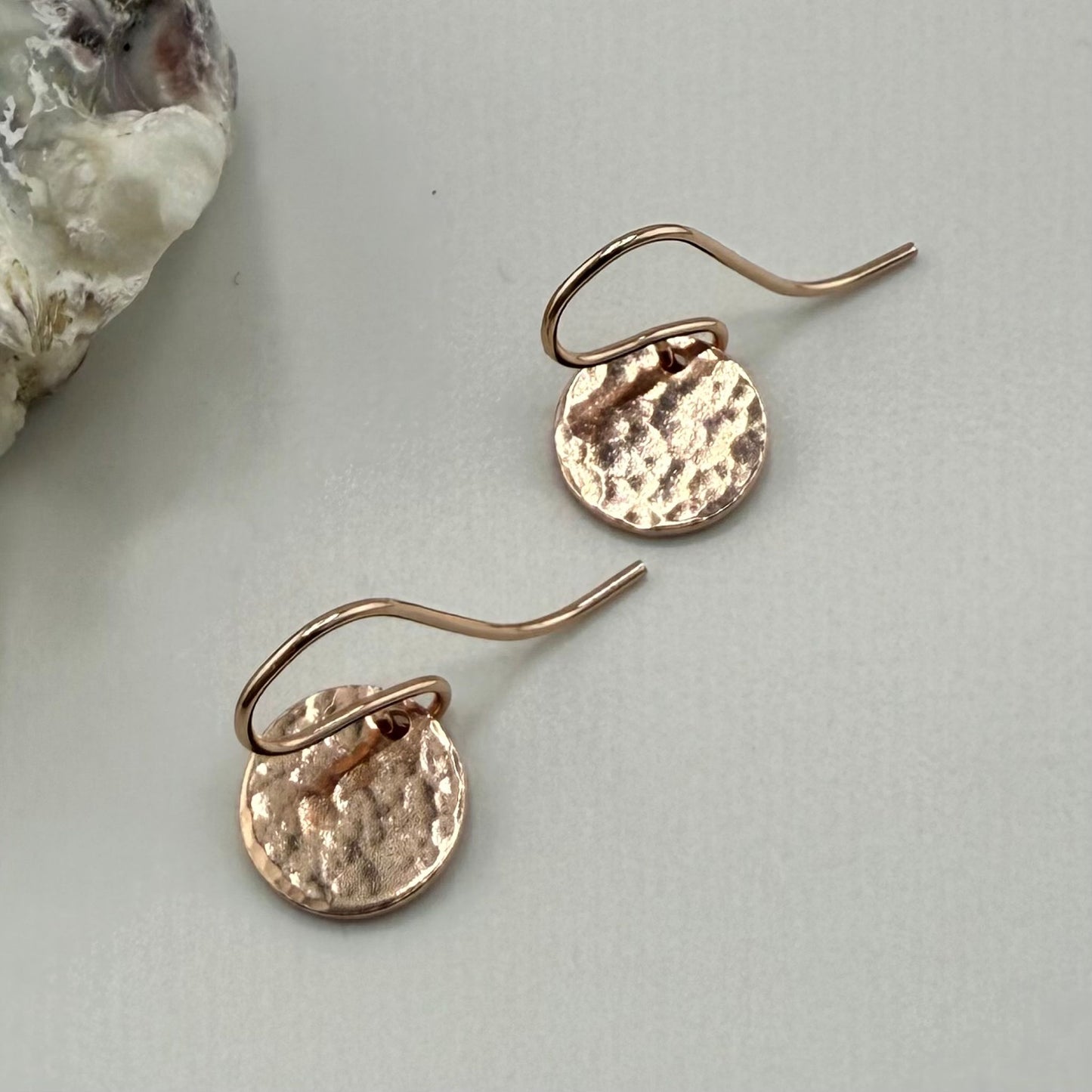Rose gold earrings on a light gray surface with a natural stone in the corner.