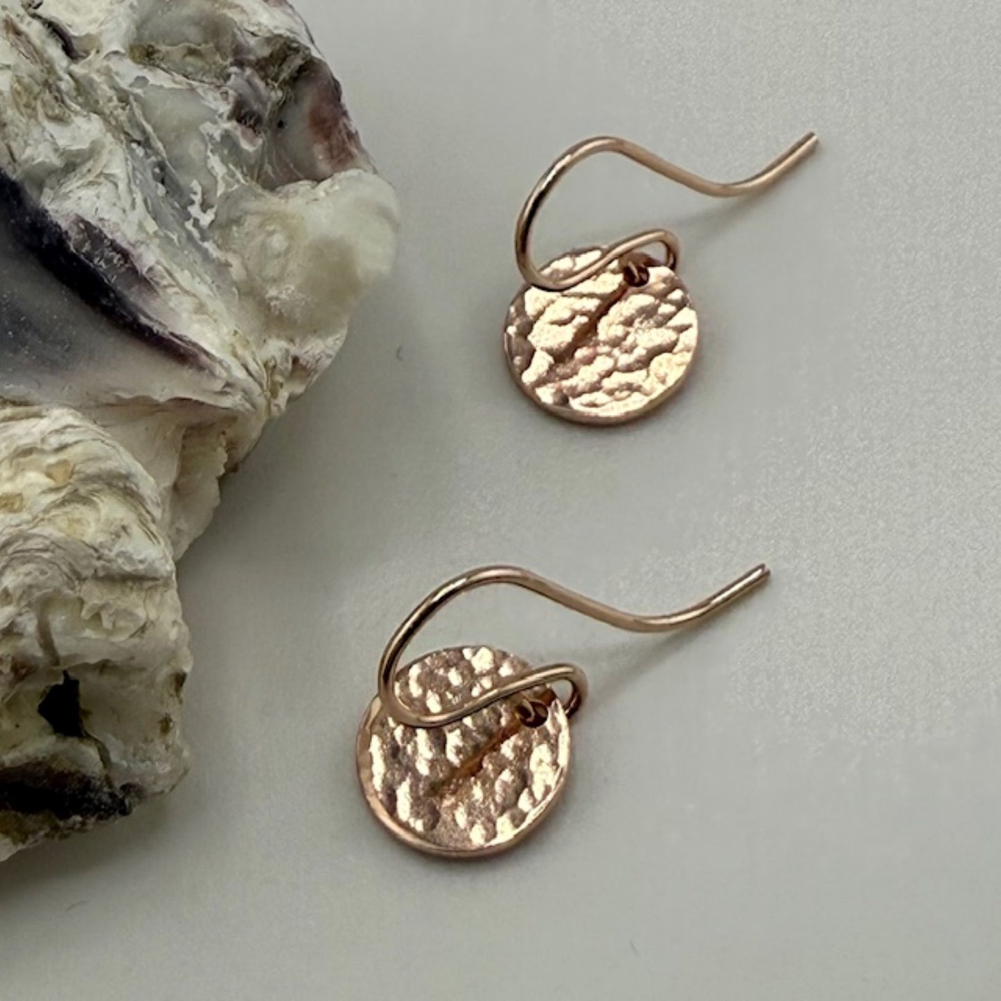 Rose gold earrings on a light gray surface with a natural rock formation.