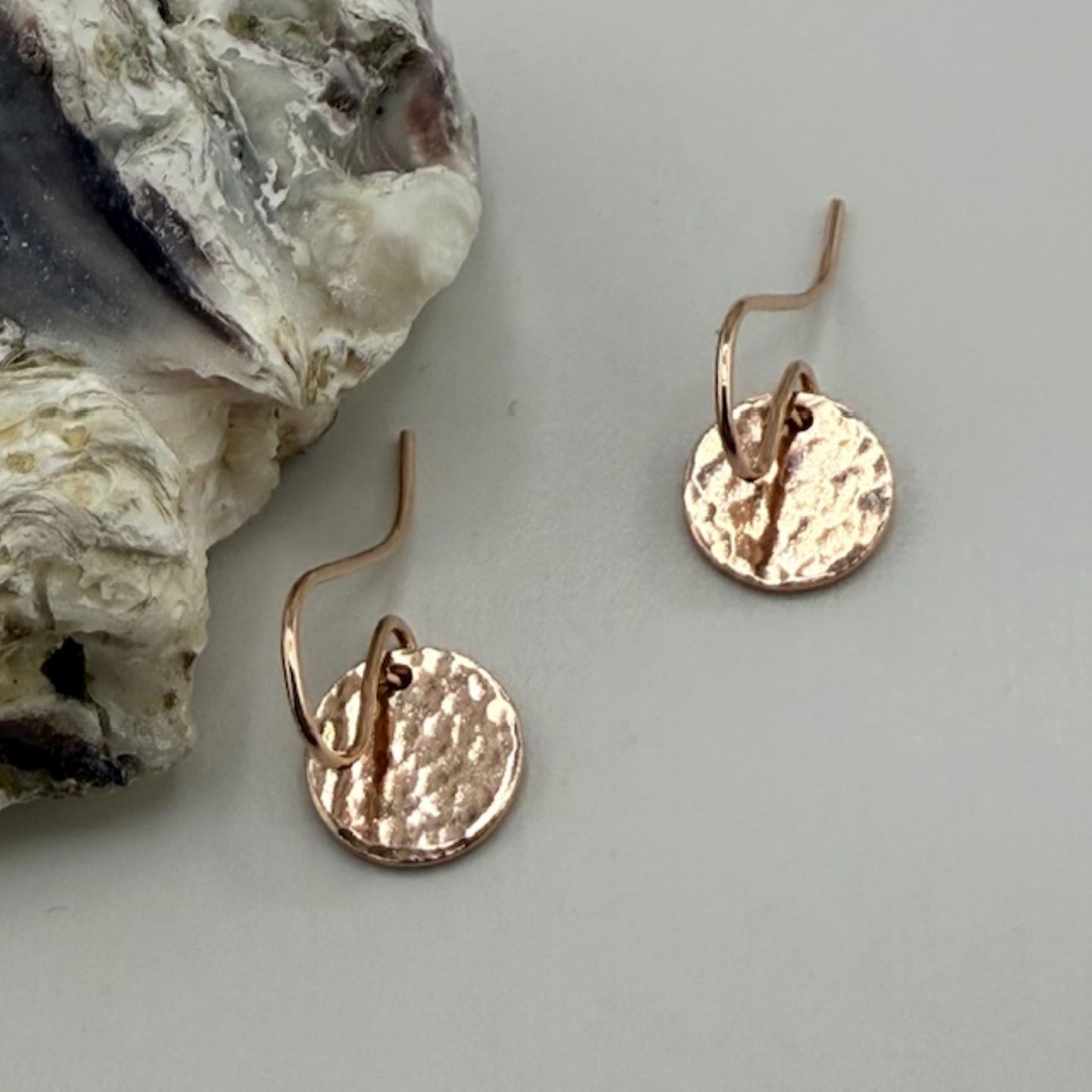 Rose gold earrings on a light gray surface with a textured rock in the background