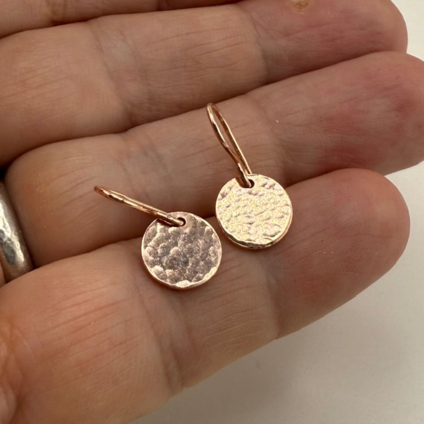 Rose gold earrings held between fingers against a neutral background