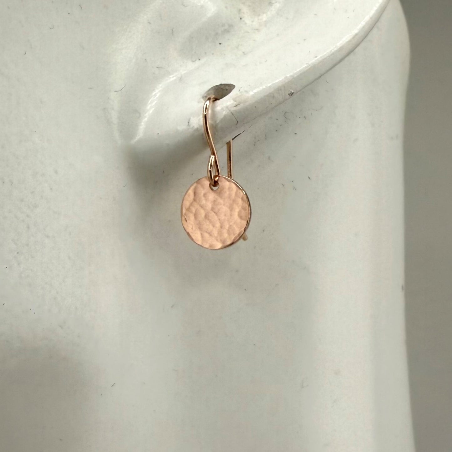 Rose gold round earring on a white earlobe display stand
