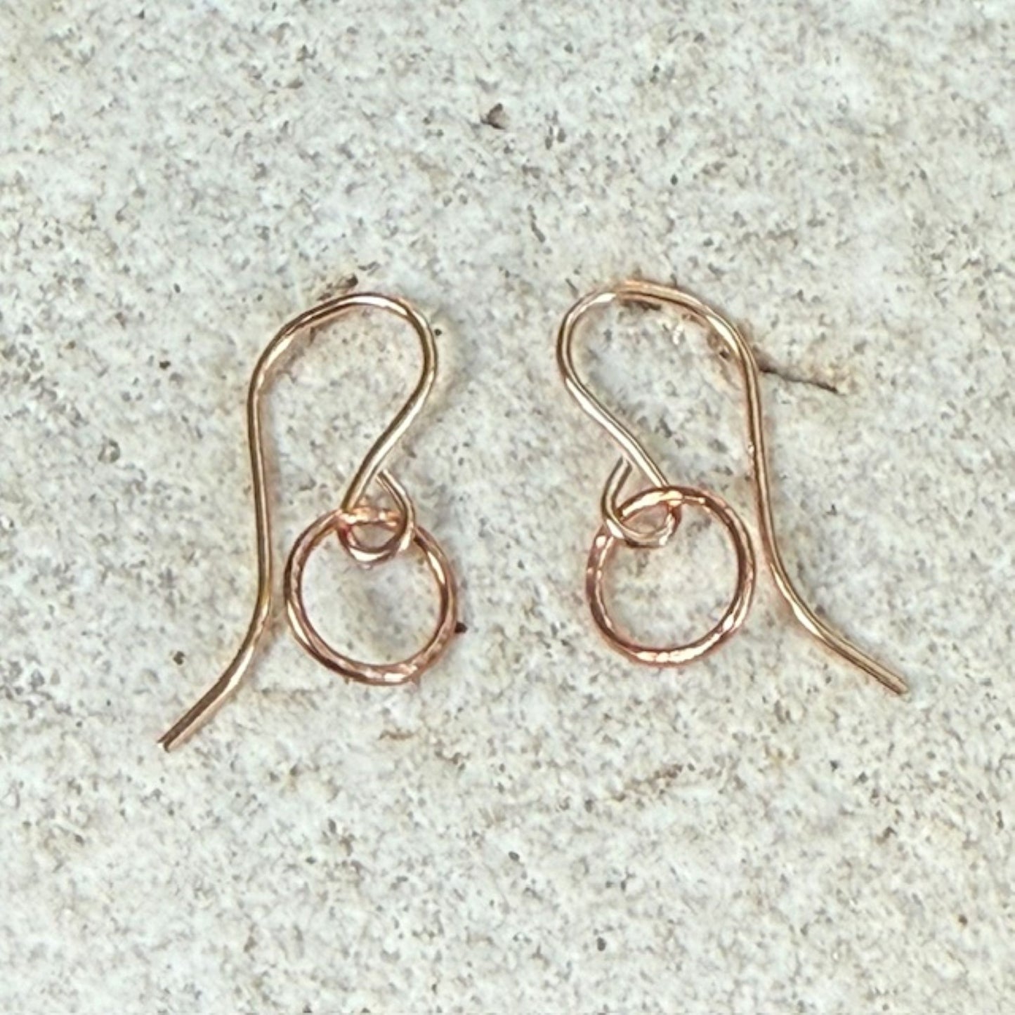 Rose gold hoop circle earrings on a textured stone surface