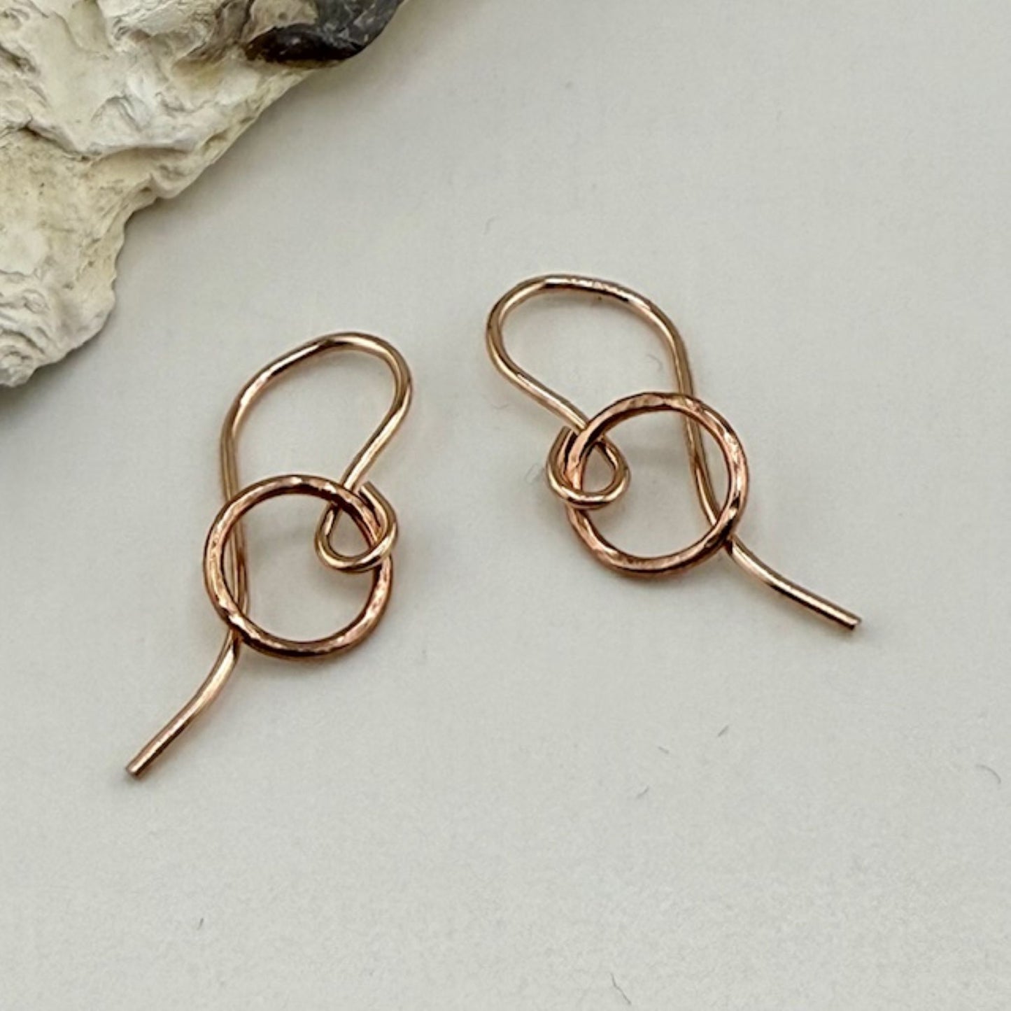 Rose gold circle hoop earrings on a light gray surface with a natural stone background