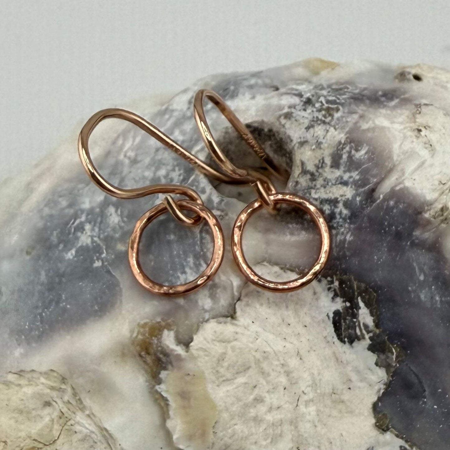 Pair of rose gold circle hoop earrings on a textured stone surface