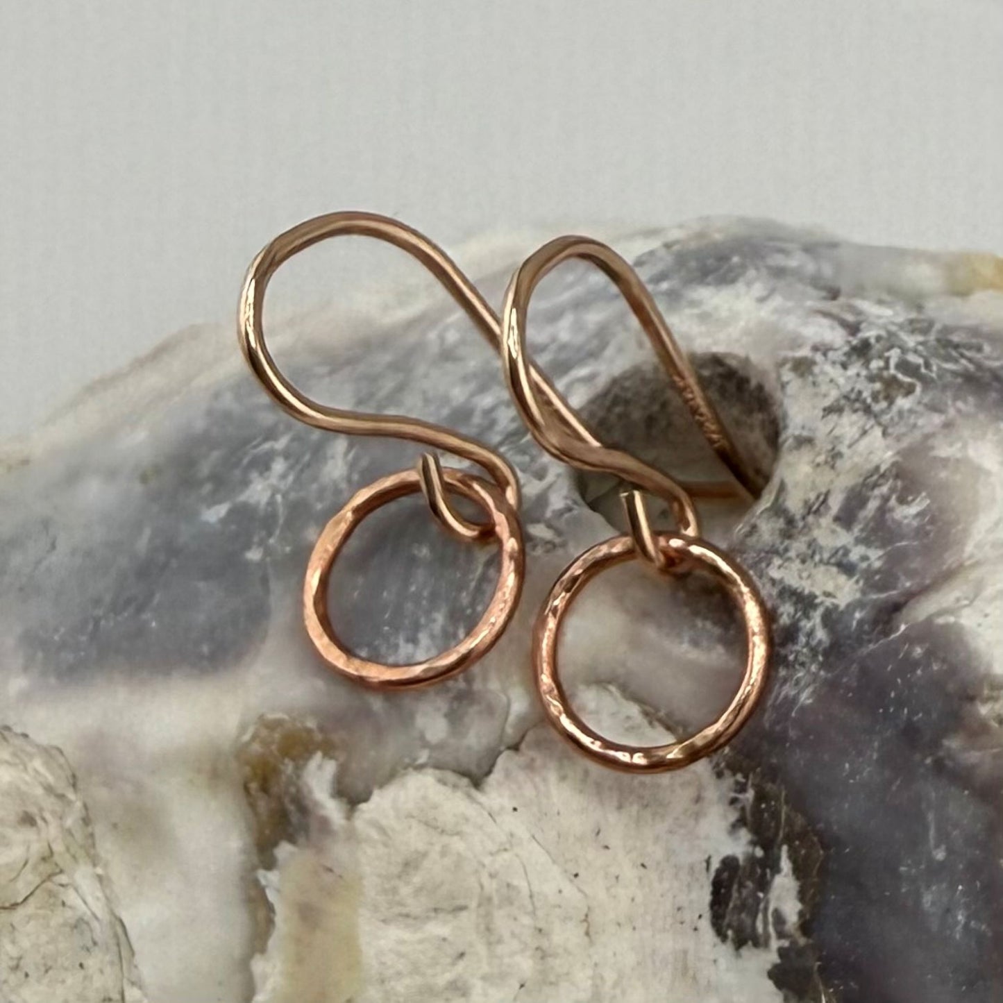 Pair of rose gold circle hoop earrings on a textured stone surface