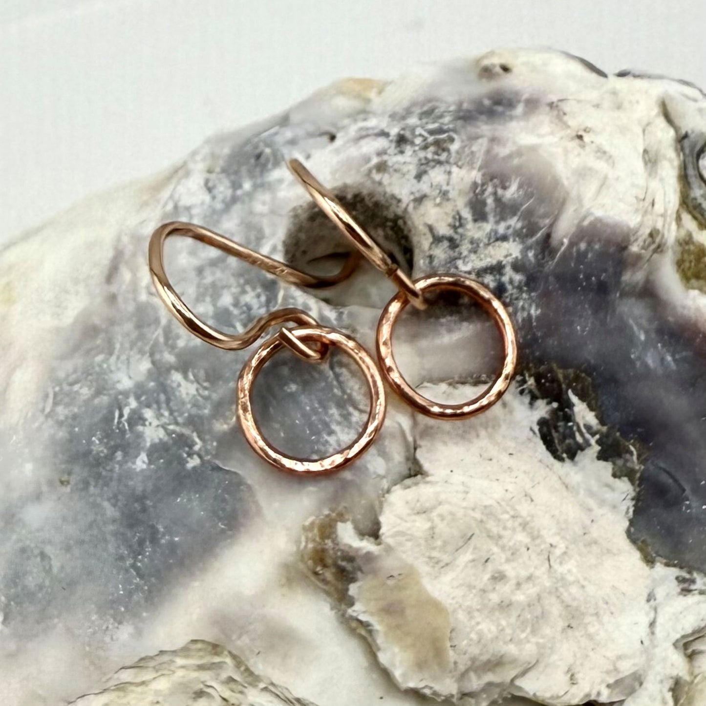 Rose gold circle hoop earrings on a textured stone surface