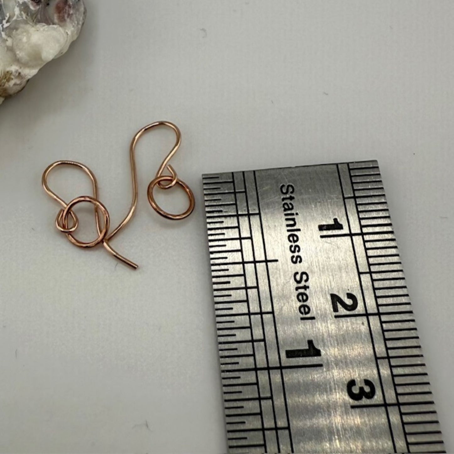 Rose gold circle hoop earrings next to a stainless steel ruler on a white surface