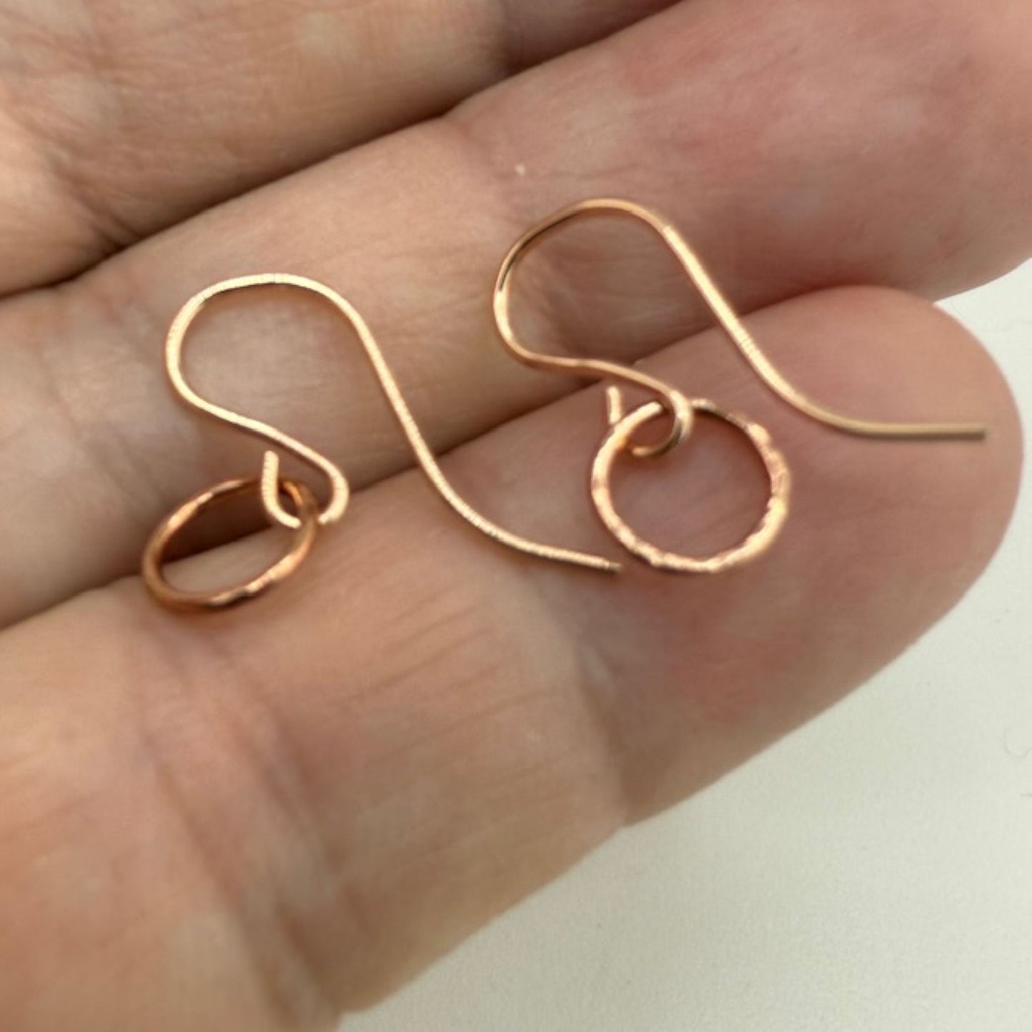 Rose gold circle hoop earrings held between fingers on a neutral background
