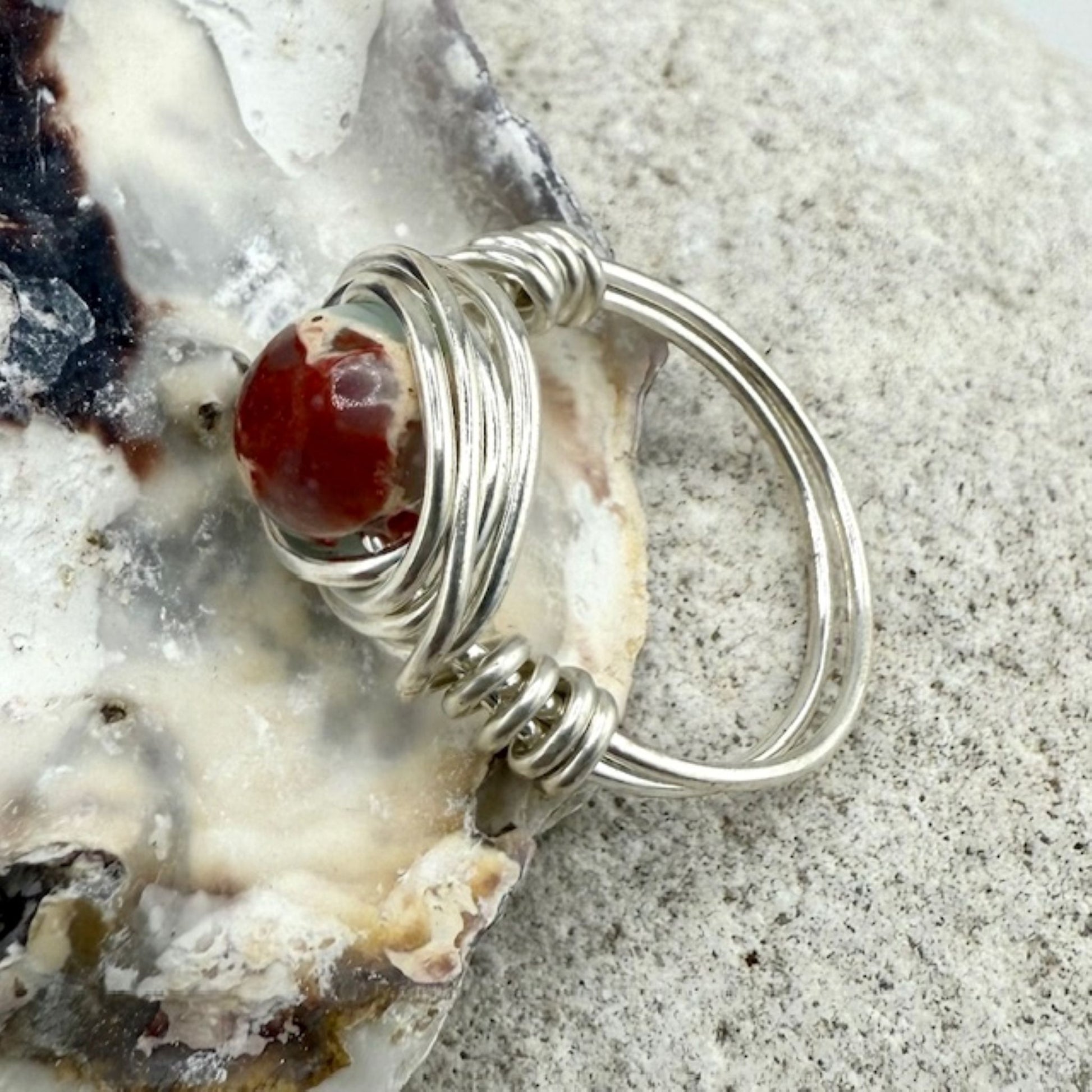 Silver wire-wrapped ring with a sea sediment jasper on a textured surface