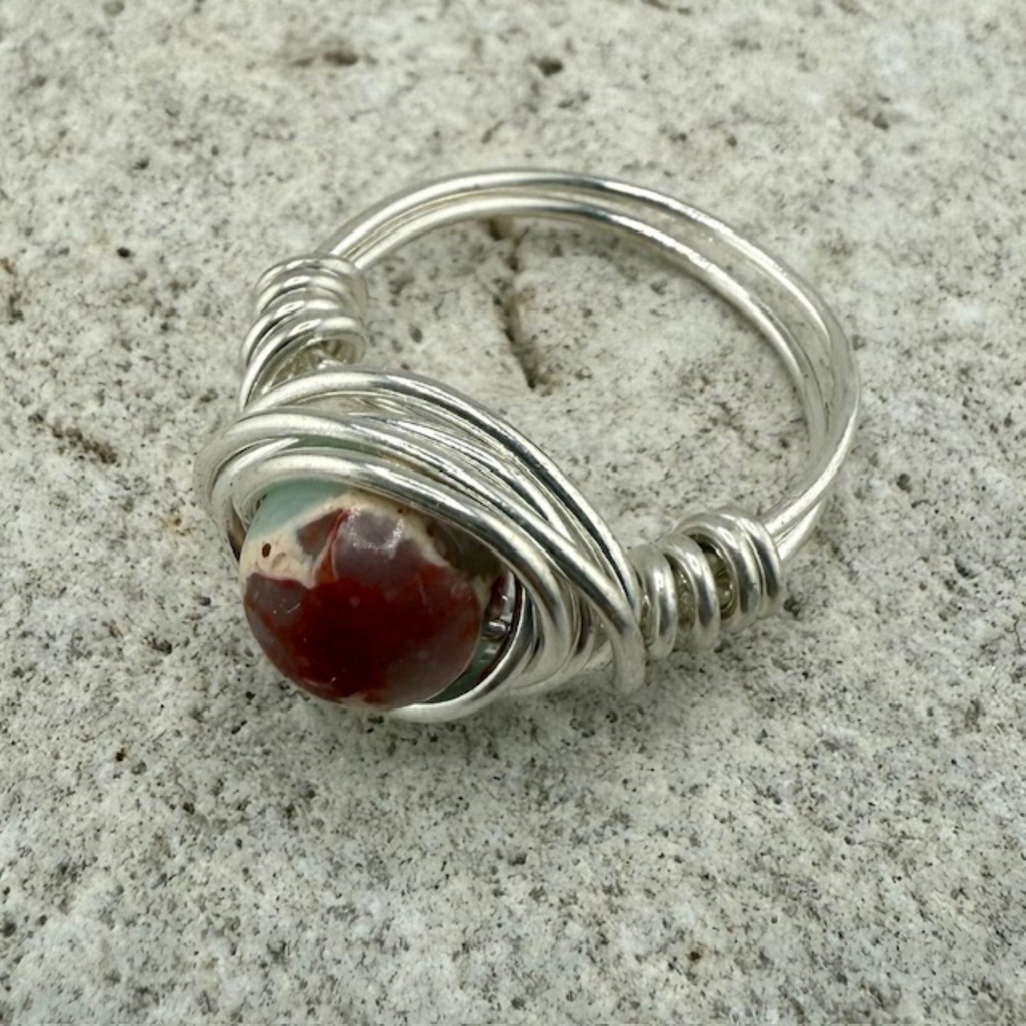 Silver wire-wrapped ring with a sea sediment jasper stone on a textured surface