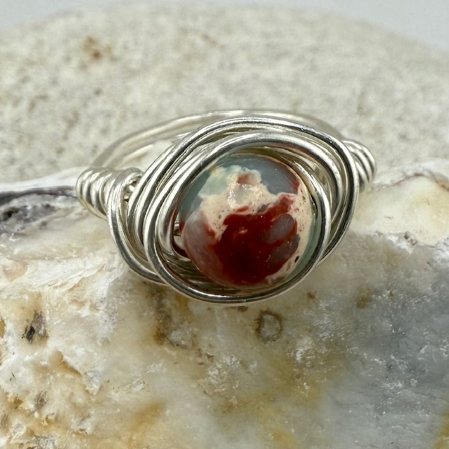 Silver wire-wrapped pendant with a sea sediment jasper stone on a textured stone background