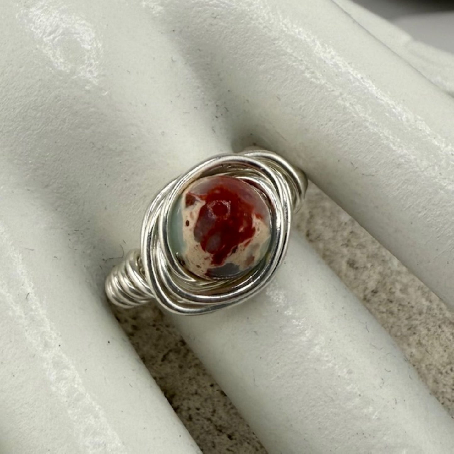 Silver ring with a sea sediment jasper stone on a white marble hand display