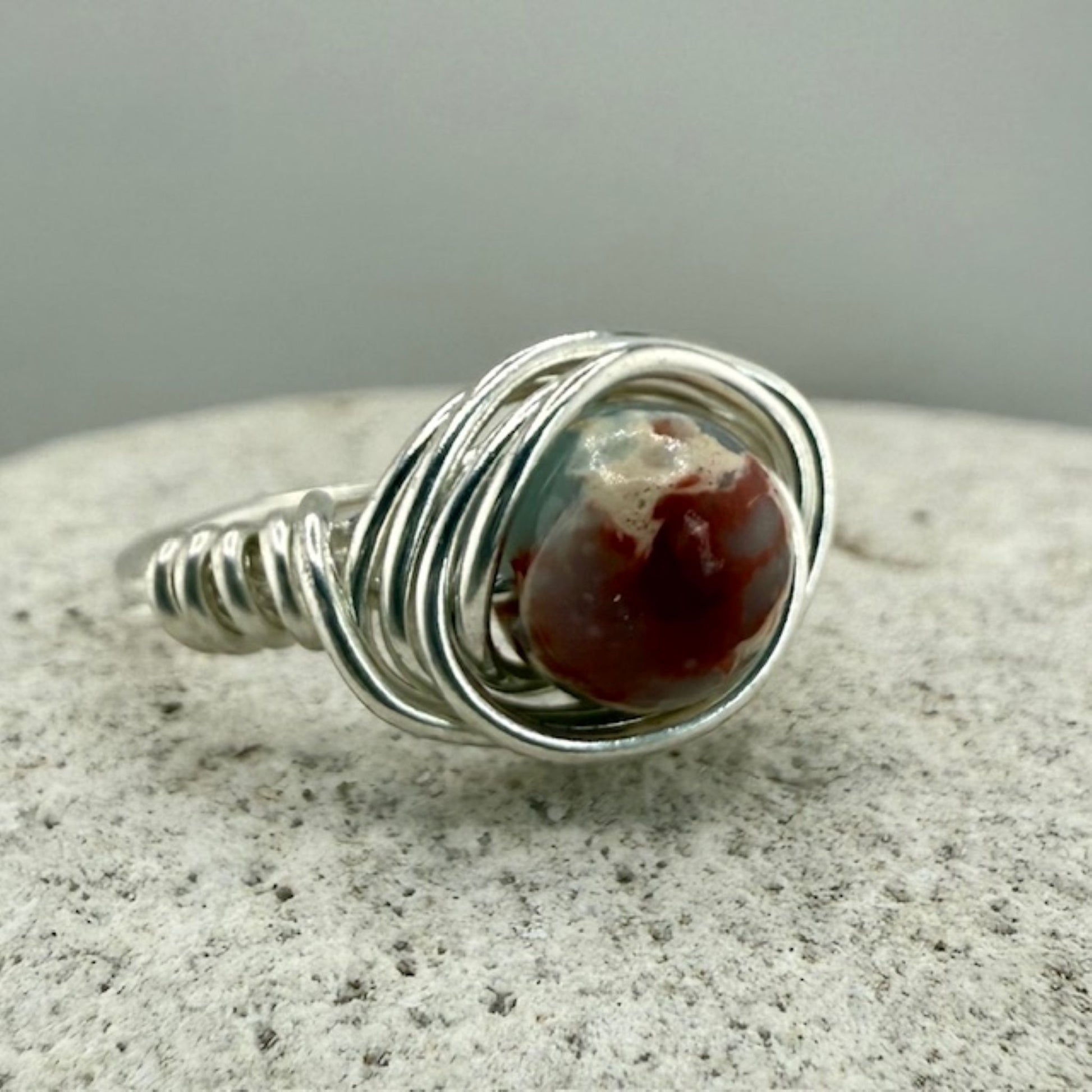 Silver wire-wrapped ring with a sea sediment jasper stone on a white stone surface