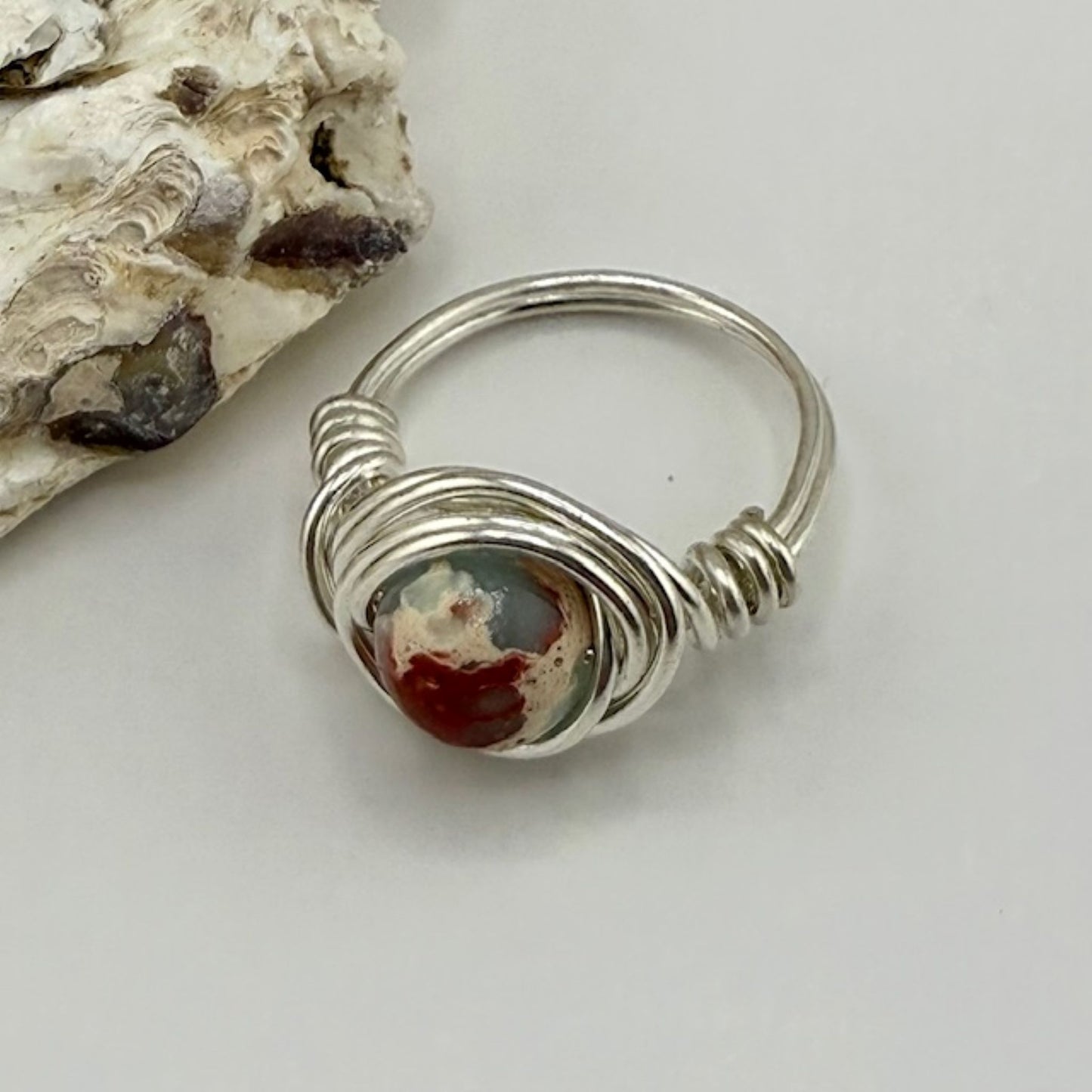 Silver wire-wrapped ring with a sea sediment jasper stone on a light background