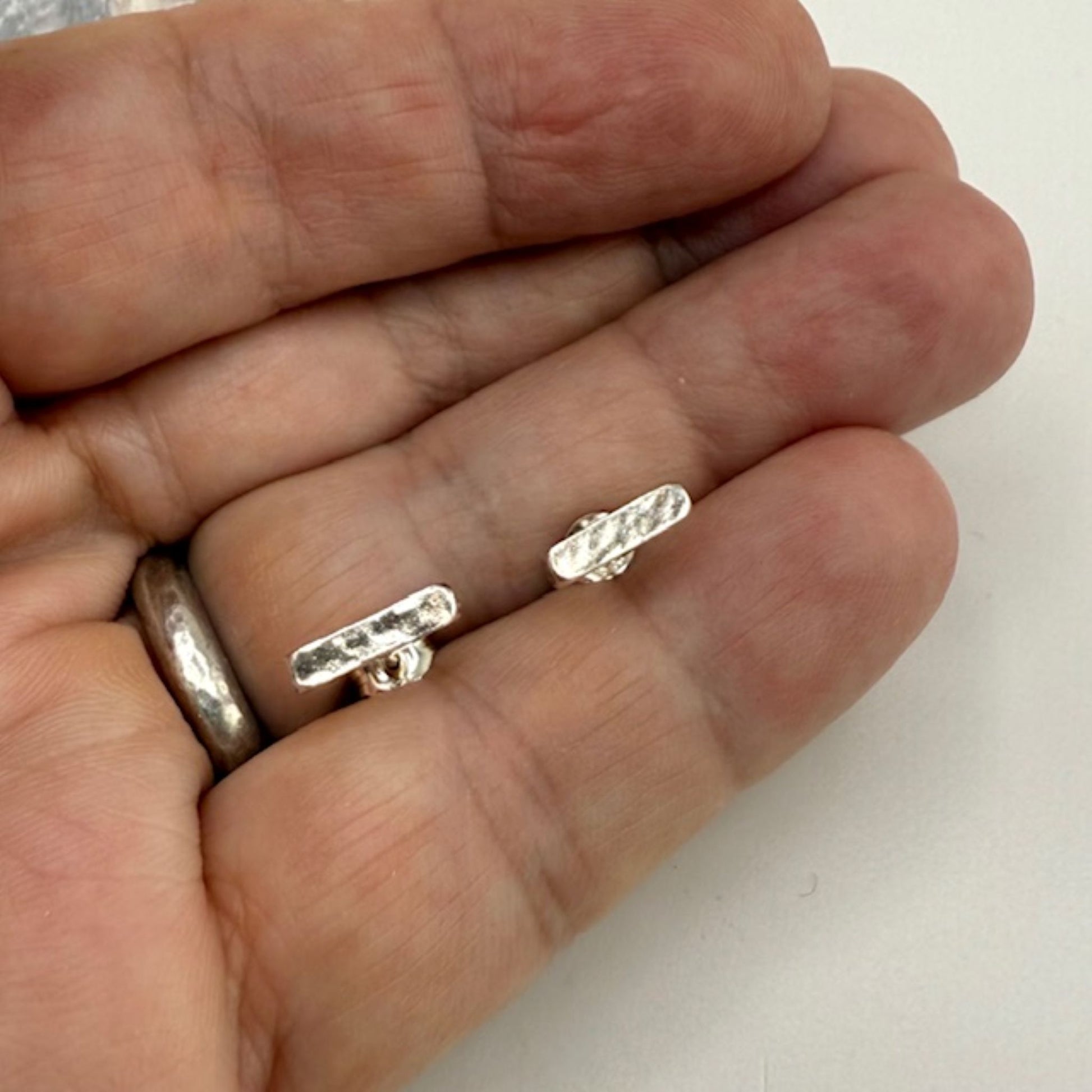 Small silver bar earrings held between fingers against a neutral background