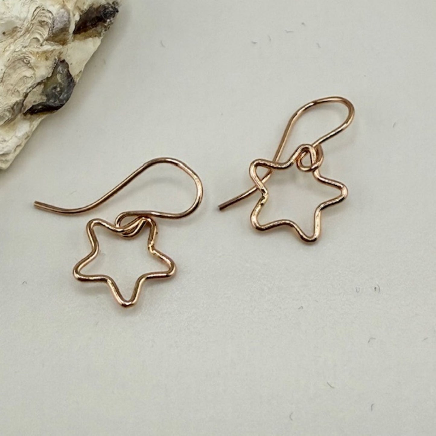 Star-shaped rose gold earrings on a light gray surface with a natural rock background.