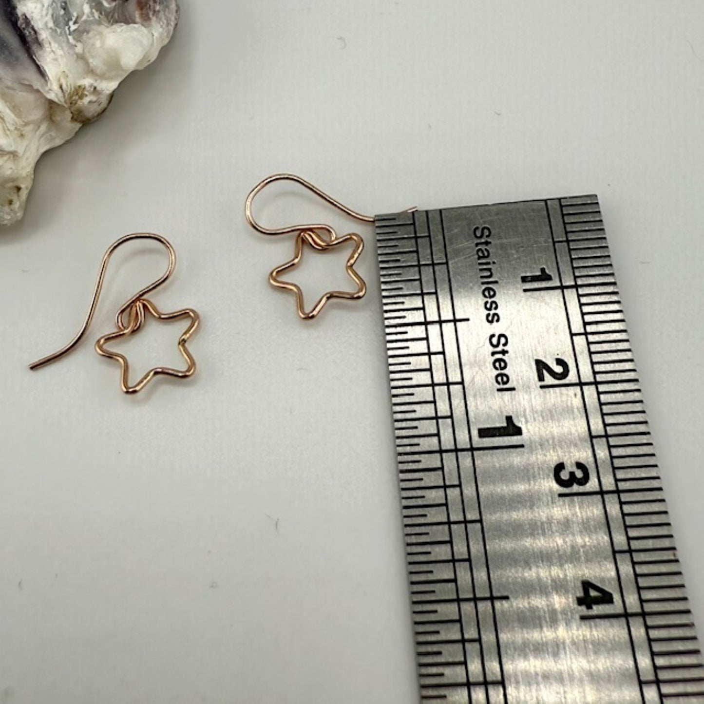 Star-shaped rose gold earrings next to a ruler on a white surface