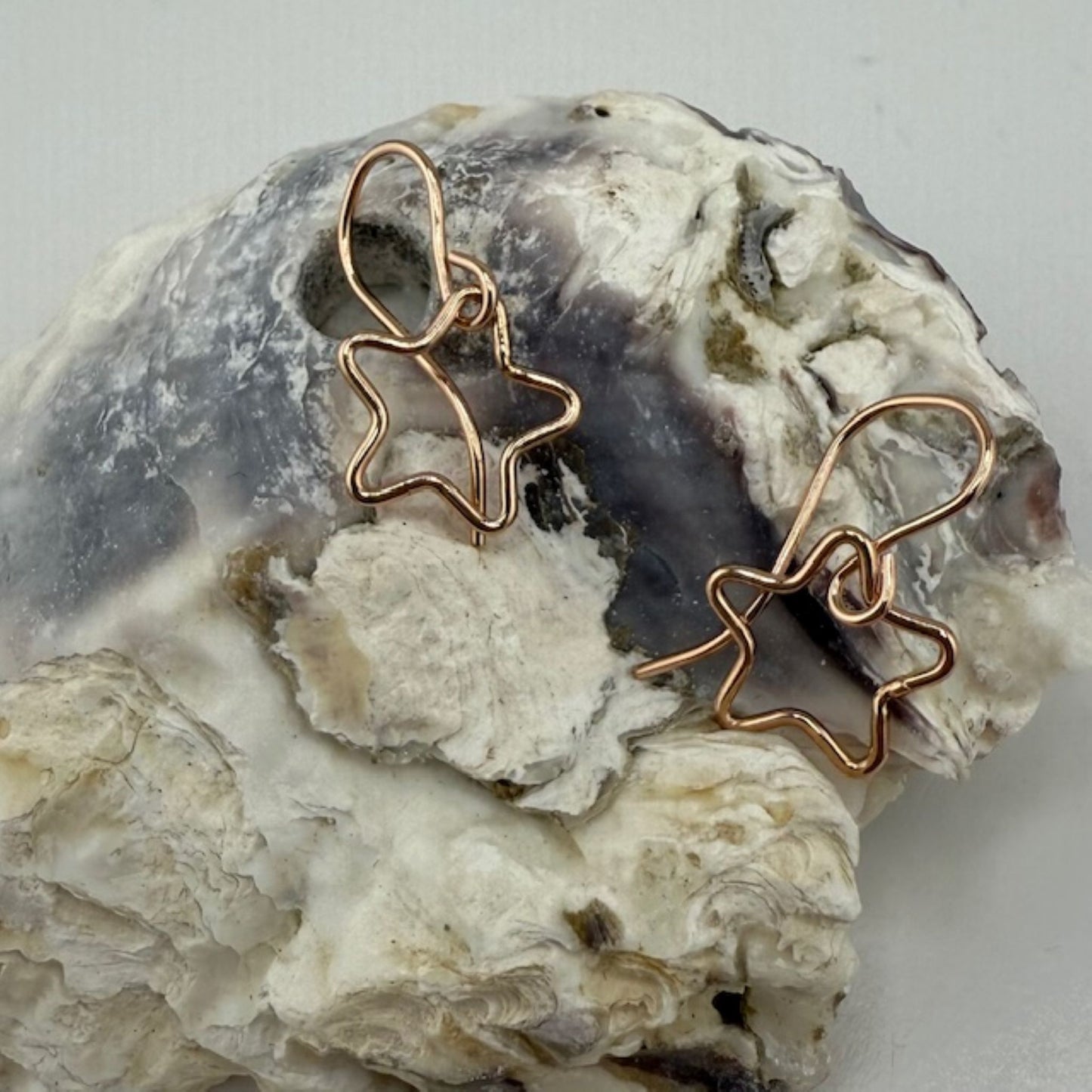 Star-shaped rose gold earrings on a textured stone surface
