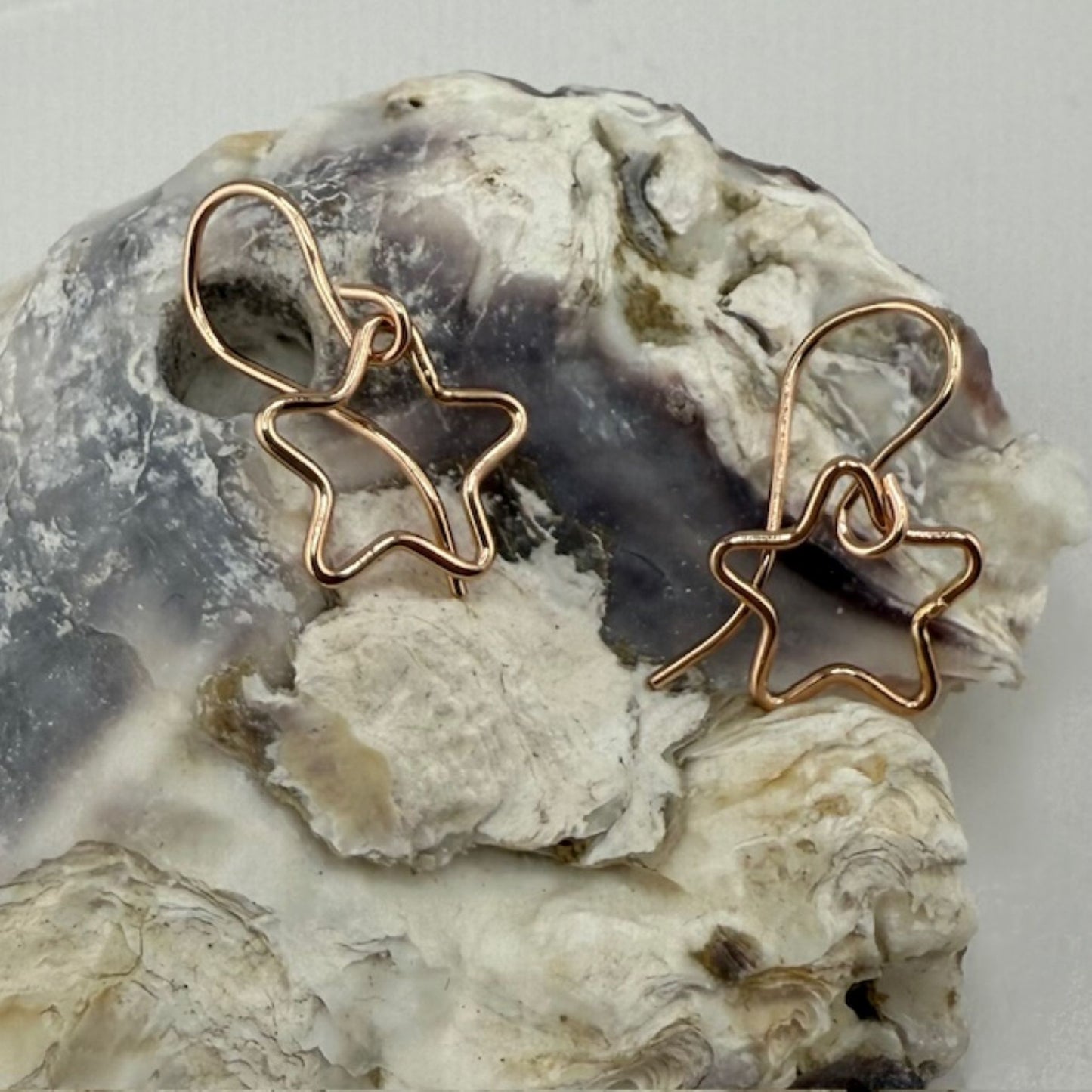 Rose gold star-shaped earrings on a textured stone surface