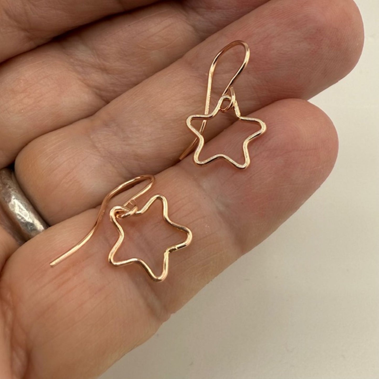 Rose gold star-shaped earrings held between fingers against a neutral background