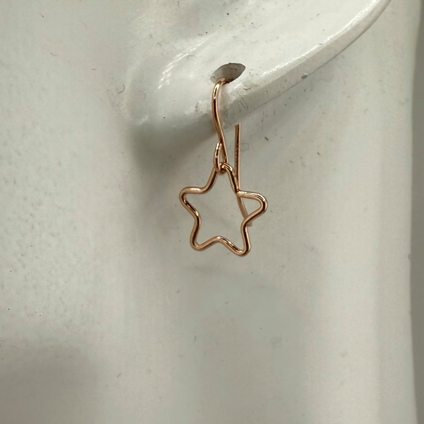 Rose gold star-shaped earring on a white ear marble display