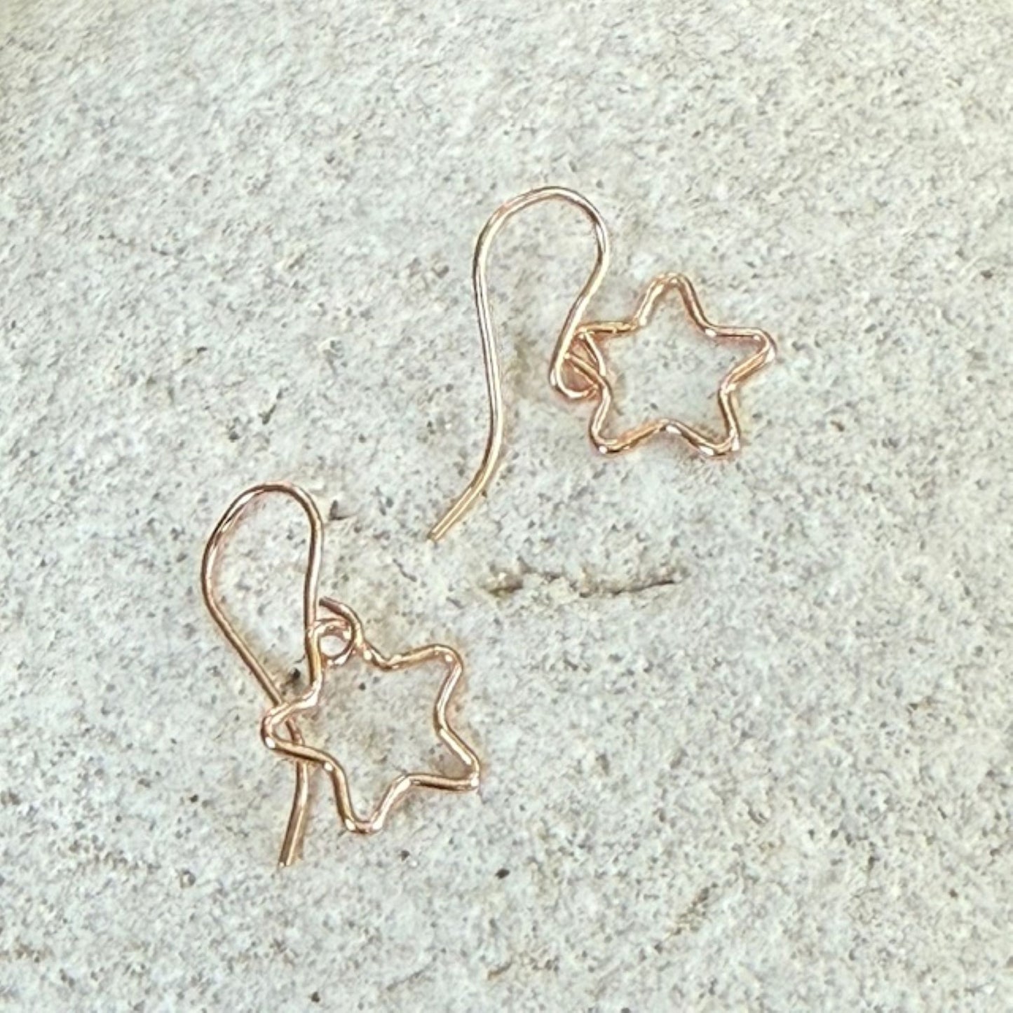 Pair of star-shaped rose gold earrings on a textured stone surface