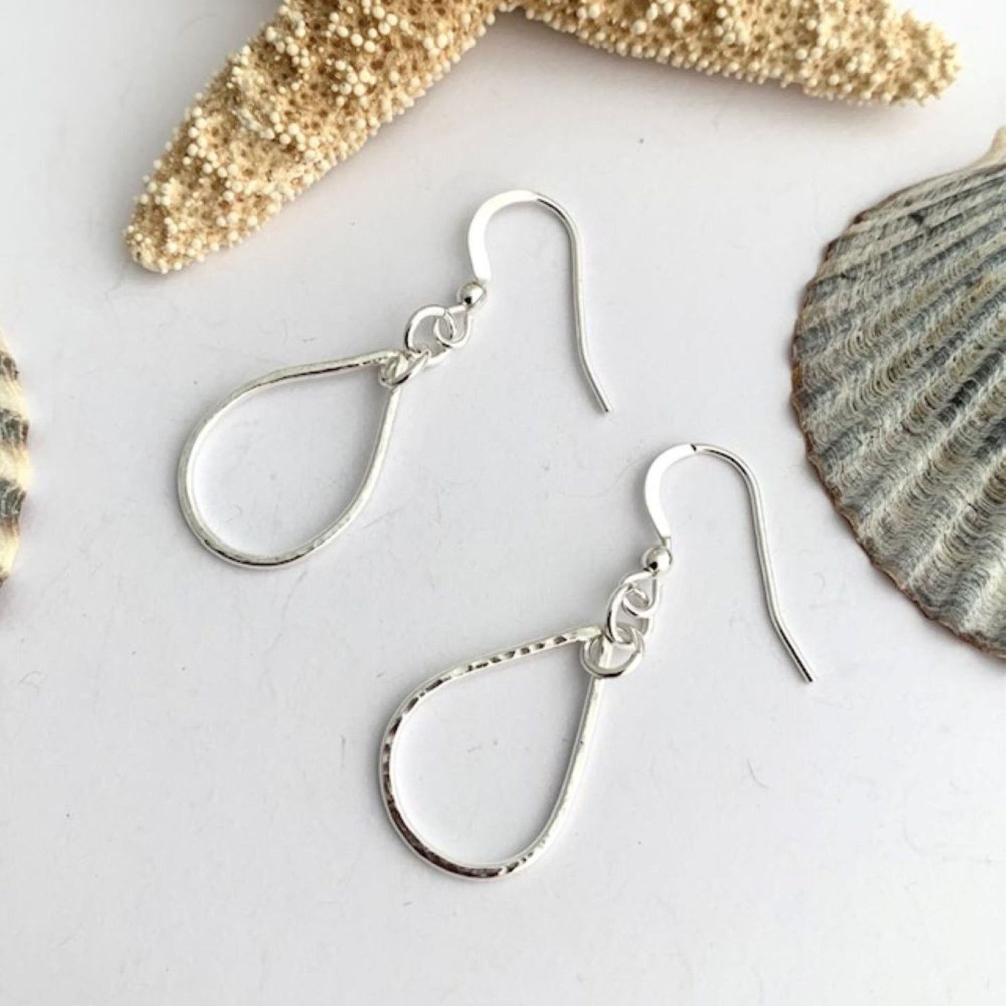 Sterling silver earrings on a light gray surface with seashells in the background