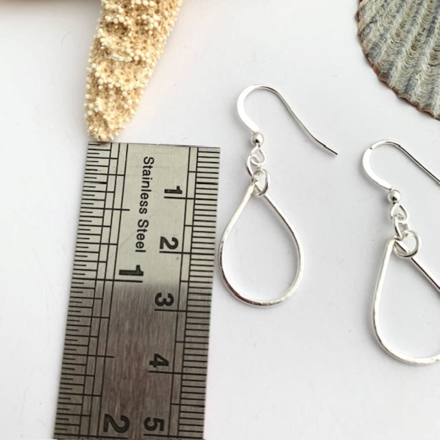 Sterling silver teardrop earrings next to a ruler on a white surface