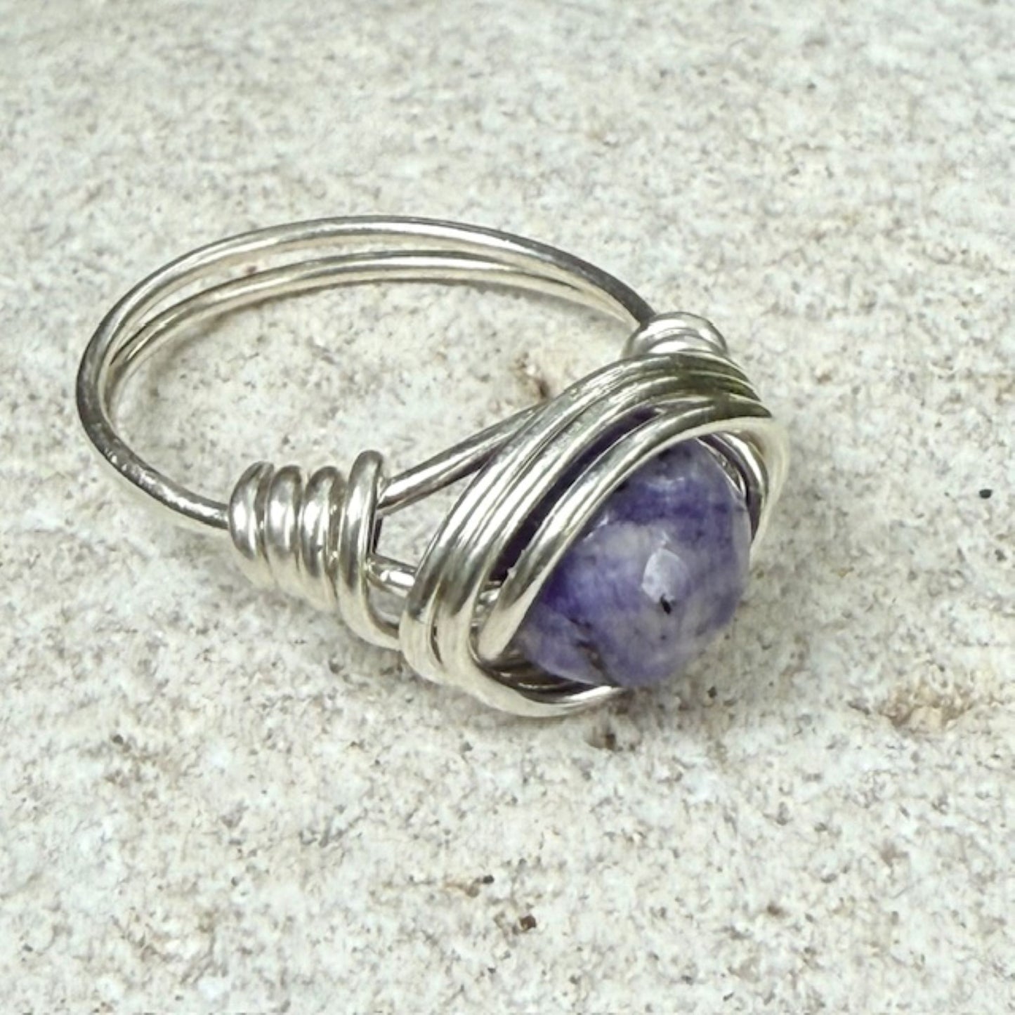 Silver wire-wrapped ring with a lapis lazuli gemstone on a textured surface