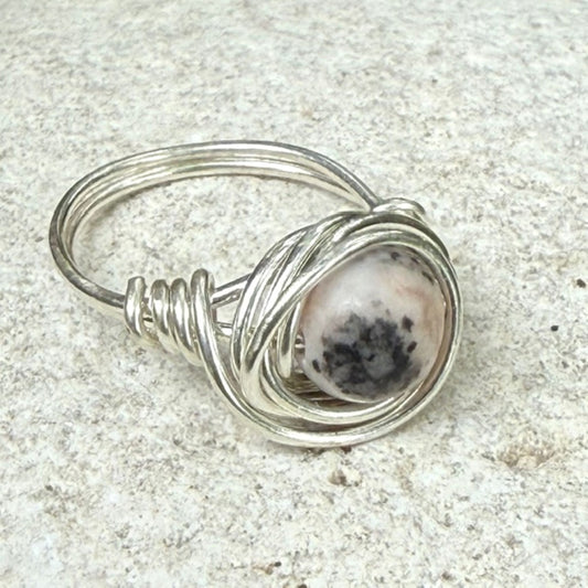 Silver wire-wrapped ring with a pink jasper gemstone on a textured surface