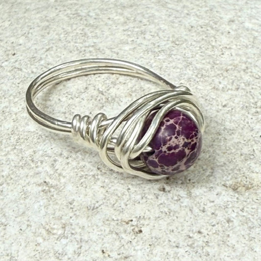 Wire wrapped purple grape jasper ring on a stone surface